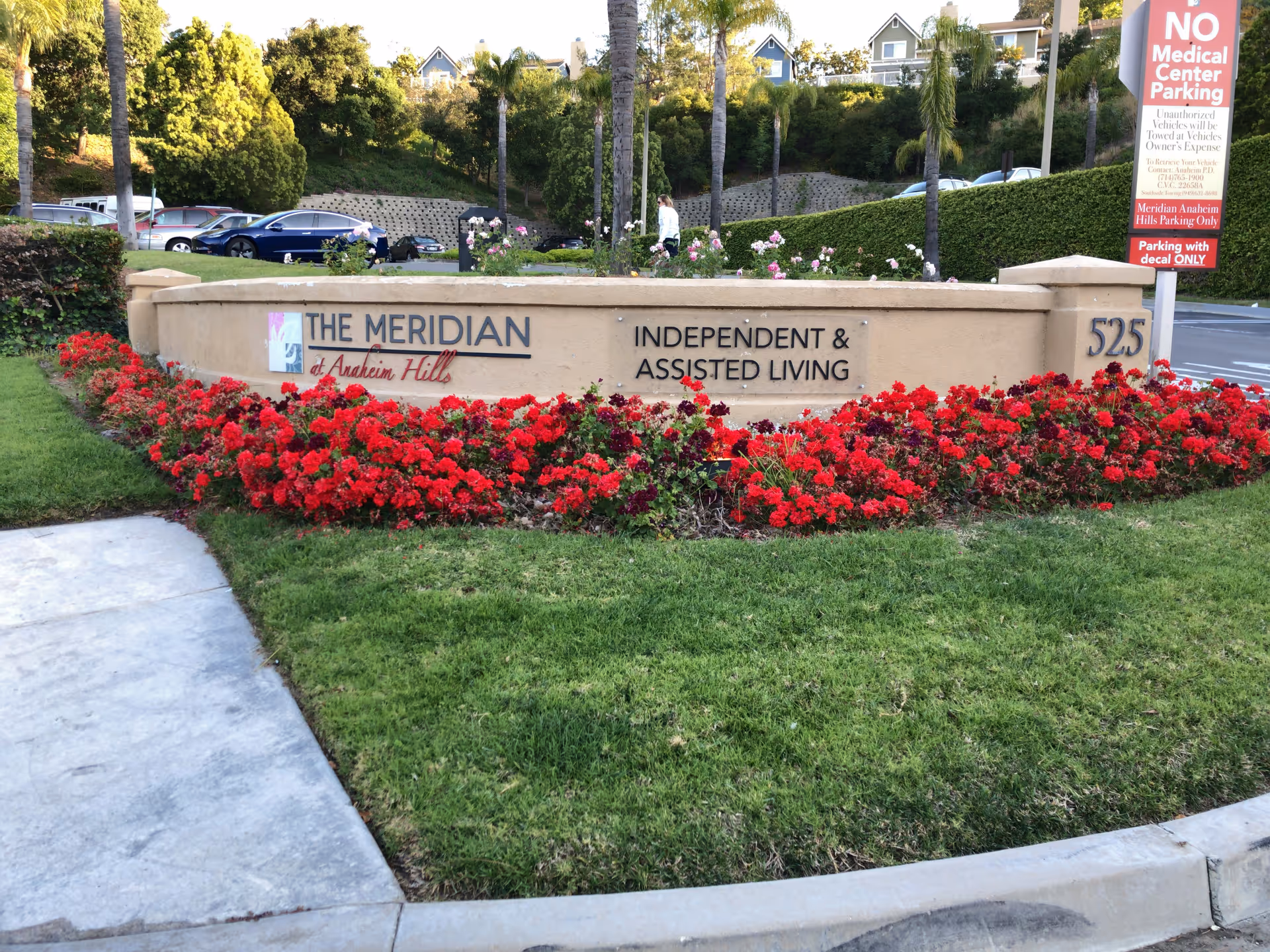 Entrance sign for The Meridian at Anaheim Hills surrounded by red flowers and greenery.