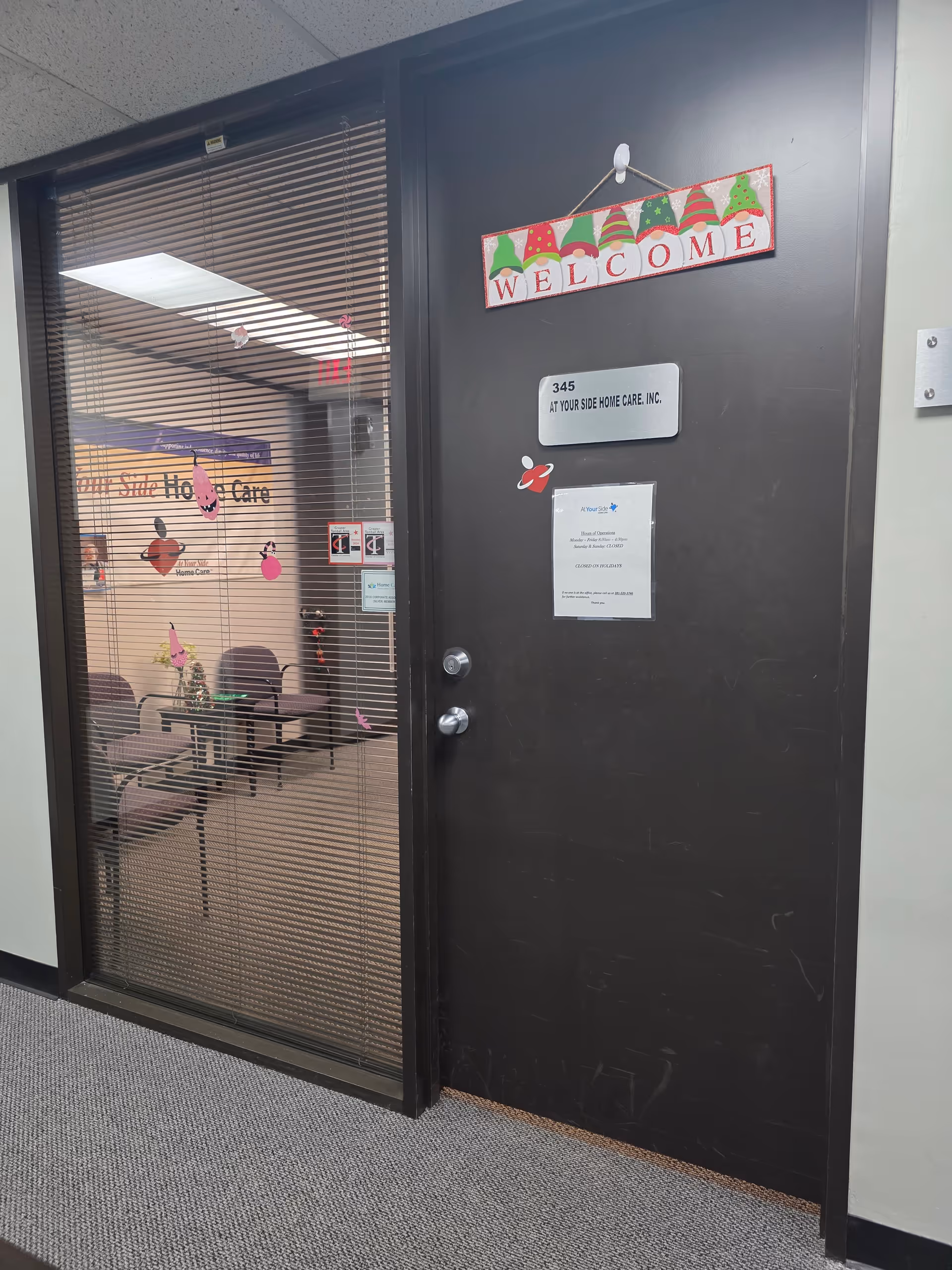 Black entrance door with a Welcome sign beside a glass-walled office and seating area.