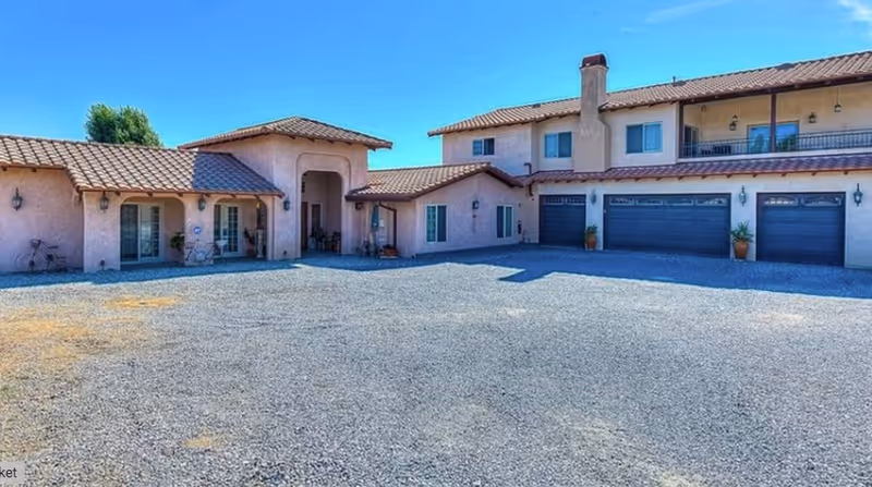 Exterior view of Hacienda Living facility with a gravel driveway and multiple garage bays.