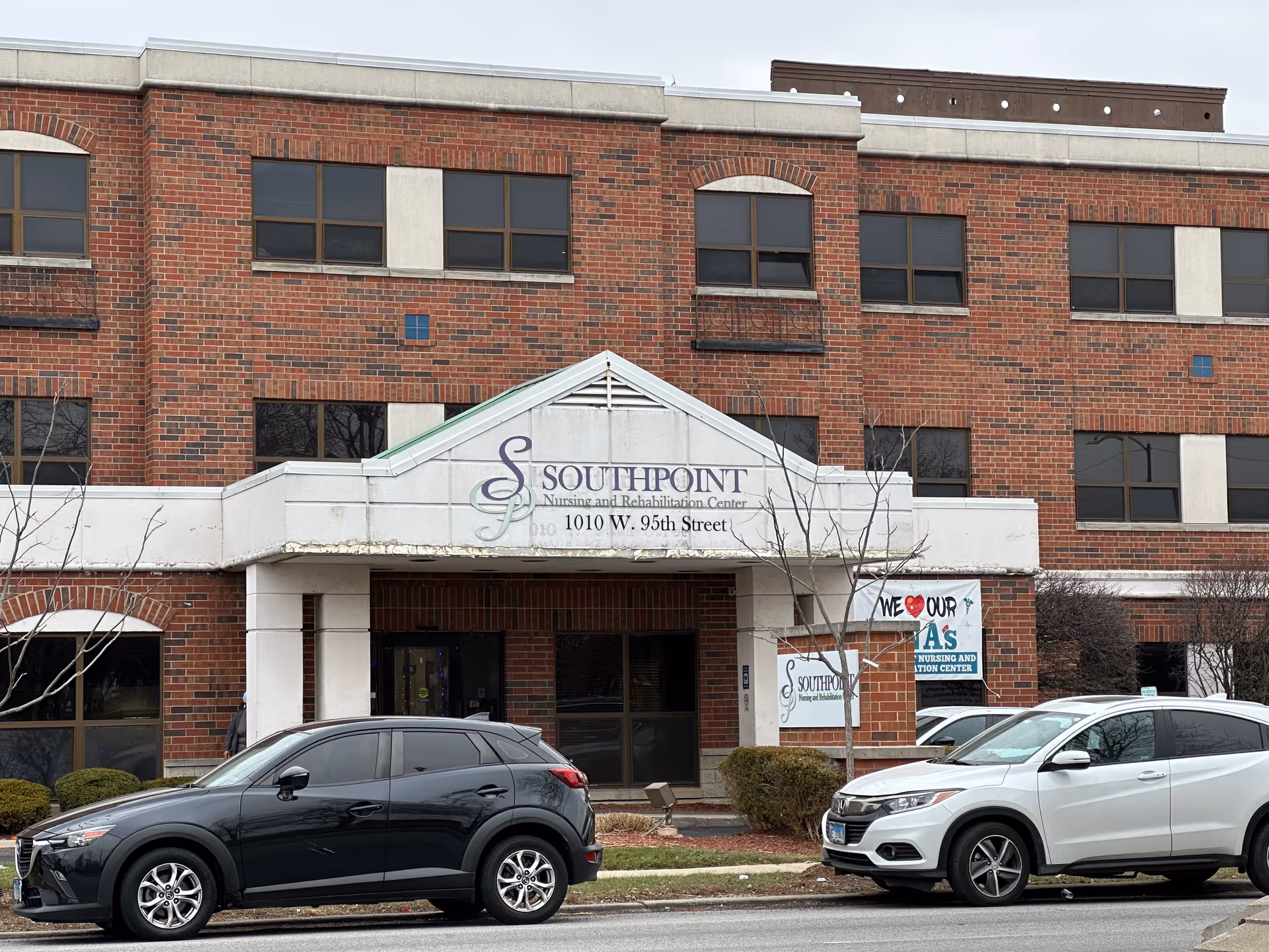 Brick facade and entrance of Southpoint Nursing and Rehabilitation Center with a canopy sign and cars parked in front.