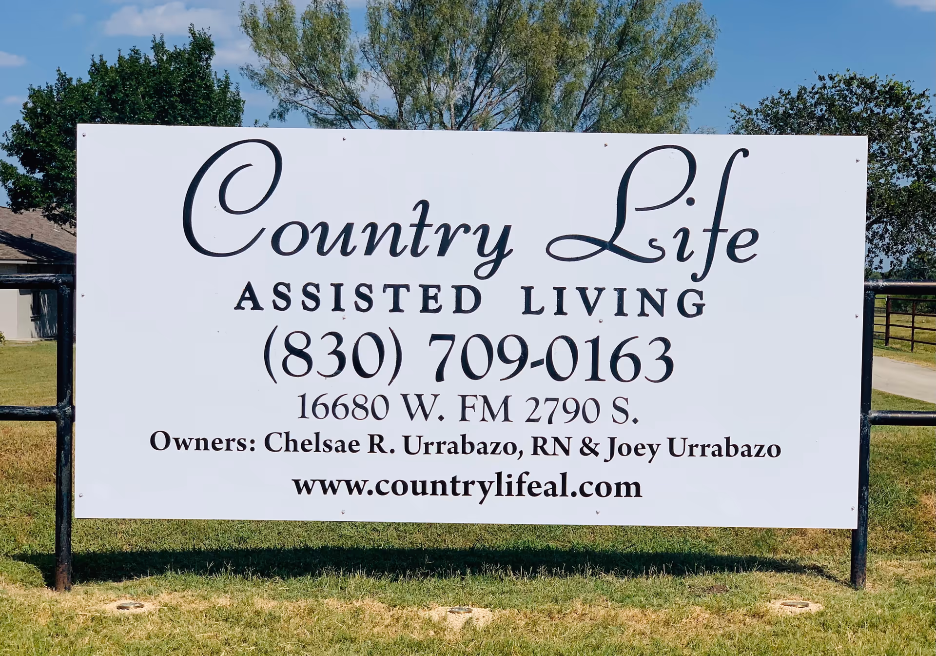 A large white sign reading Country Life Assisted Living, with contact details on a grassy lot.