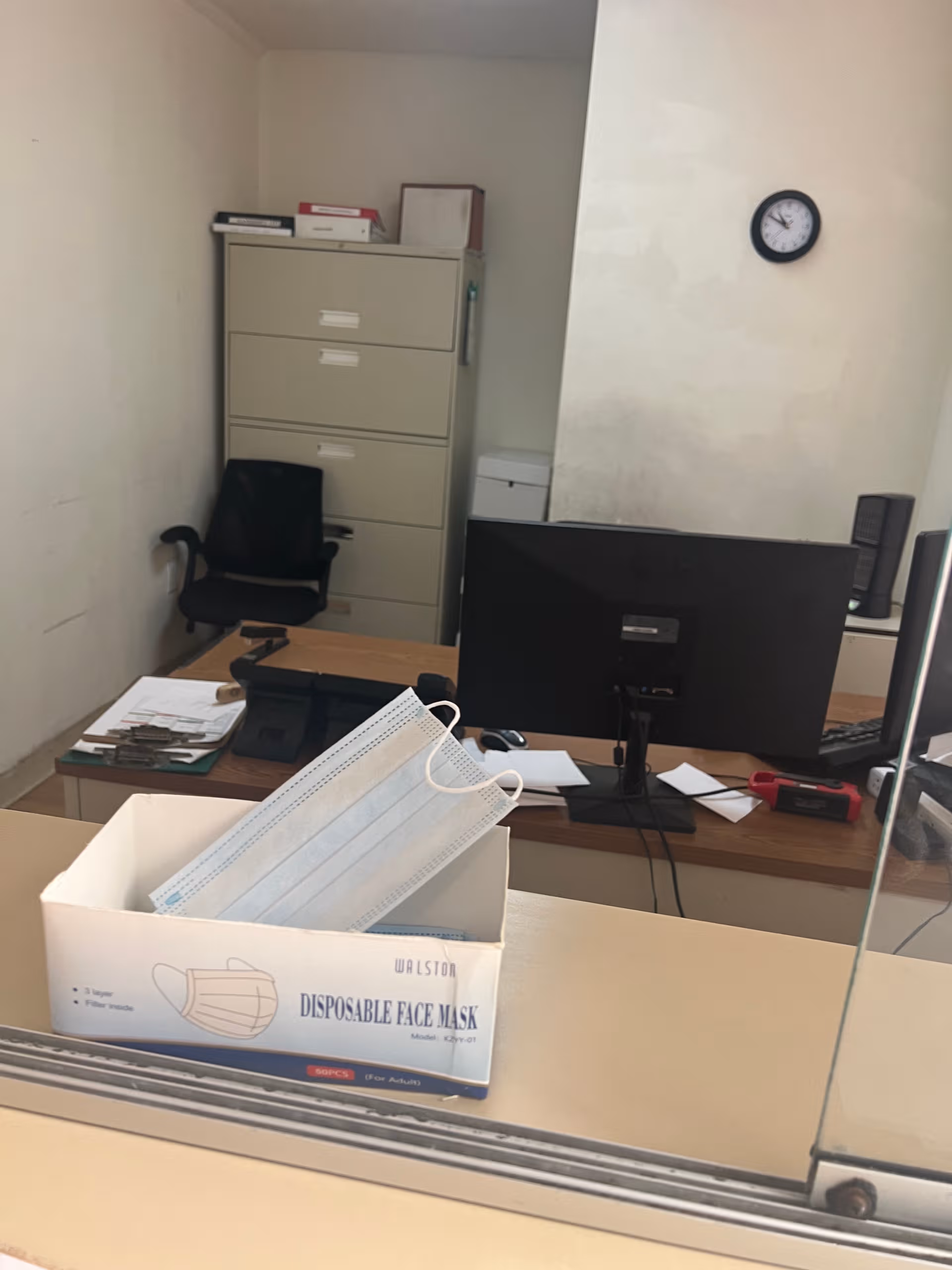 Office reception area with computer monitor, filing cabinet, boxes, and a box of disposable face masks.
