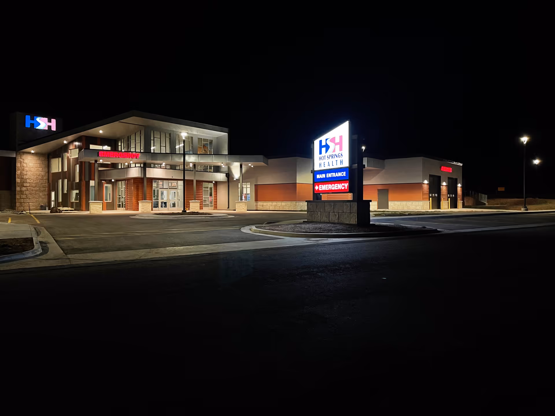 Night view of Hot Springs Health building front with illuminated sign and parking.