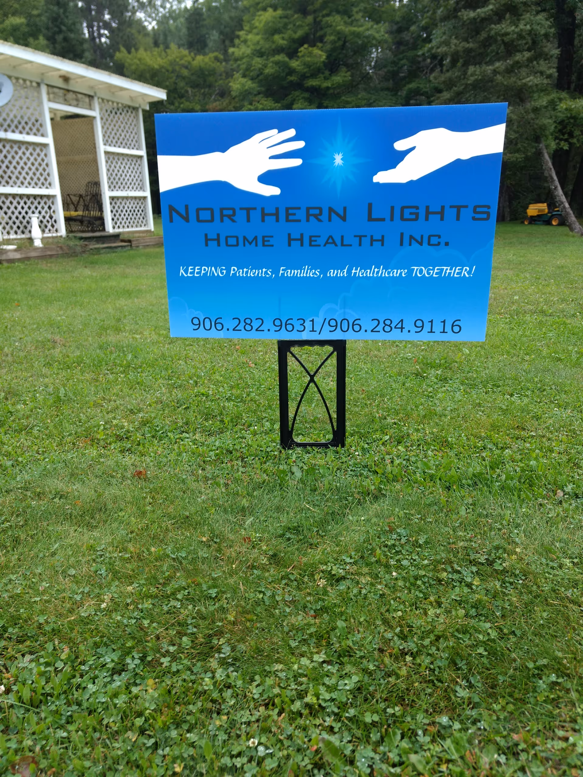 Blue Northern Lights Home Health sign on a grassy lawn near a white building.