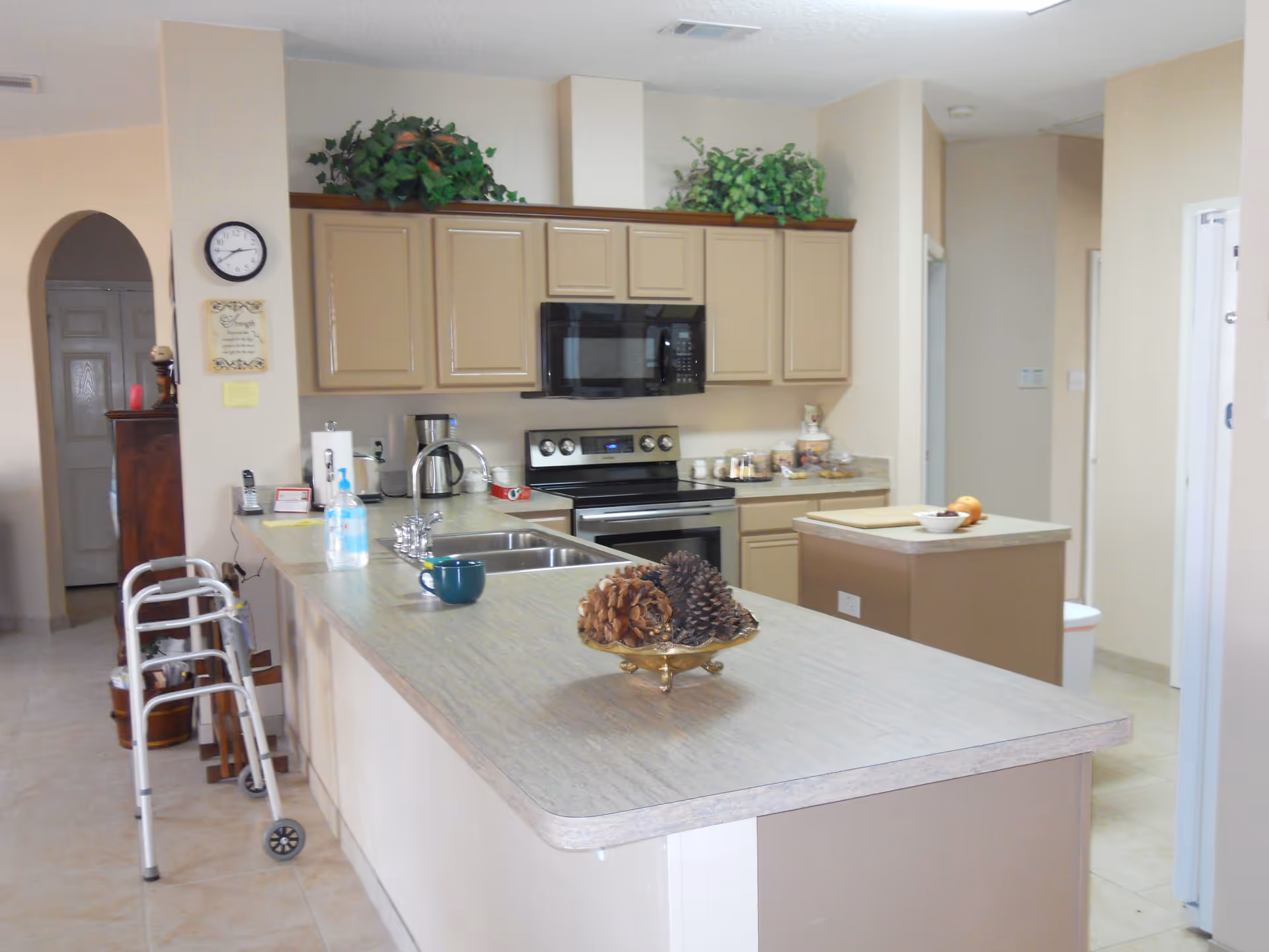 Open kitchen with a large island countertop, sink, stove, upper cabinets, and a walker parked nearby.