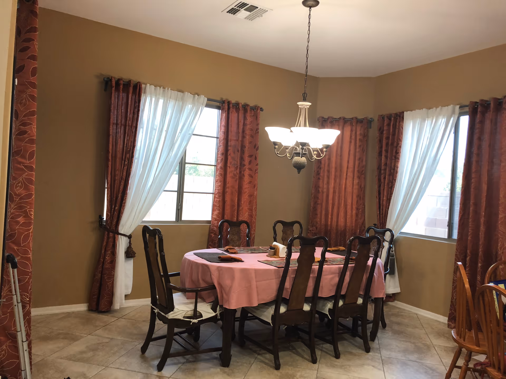 Dining room with a round pink tablecloth, wooden chairs, and a chandelier.