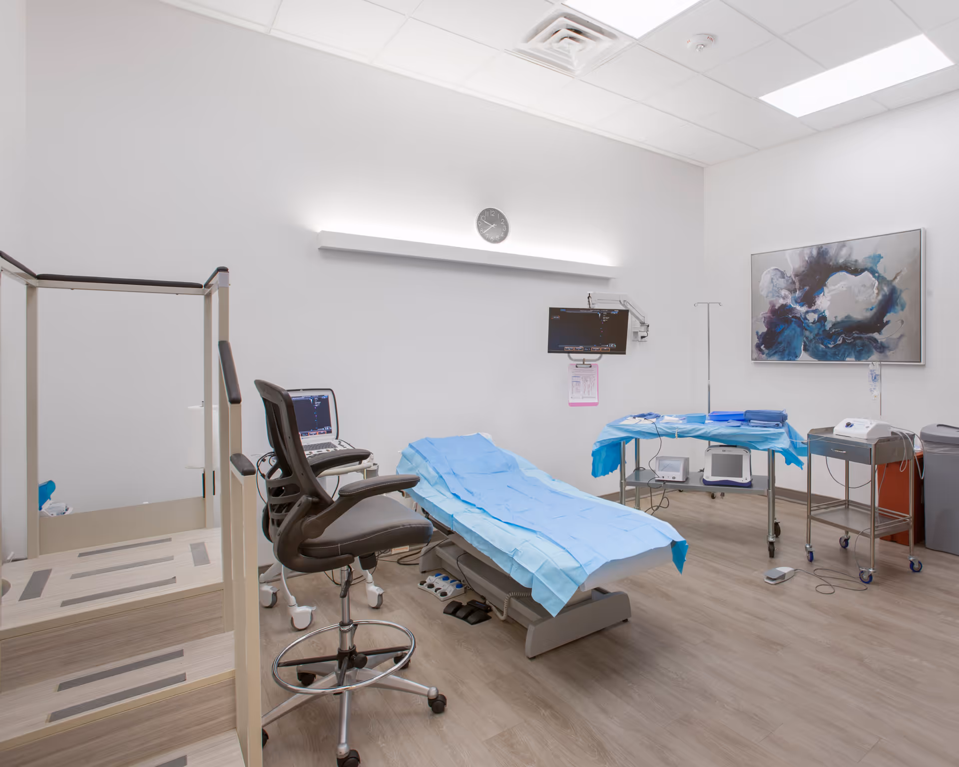 A medical procedure room with an examination bed, blue drapes, and medical equipment.