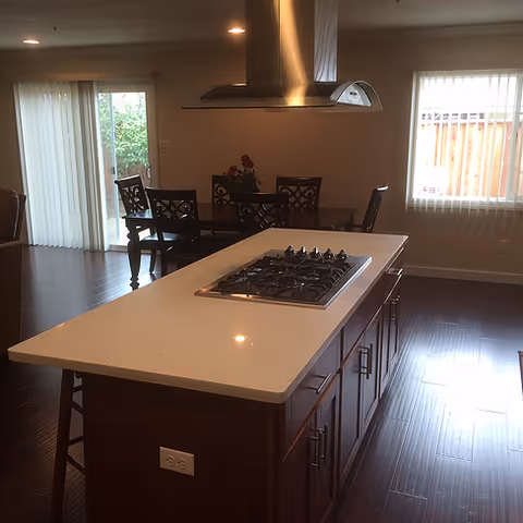 Modern kitchen with island, stainless range hood, and dark wood cabinets, adjacent dining area.
