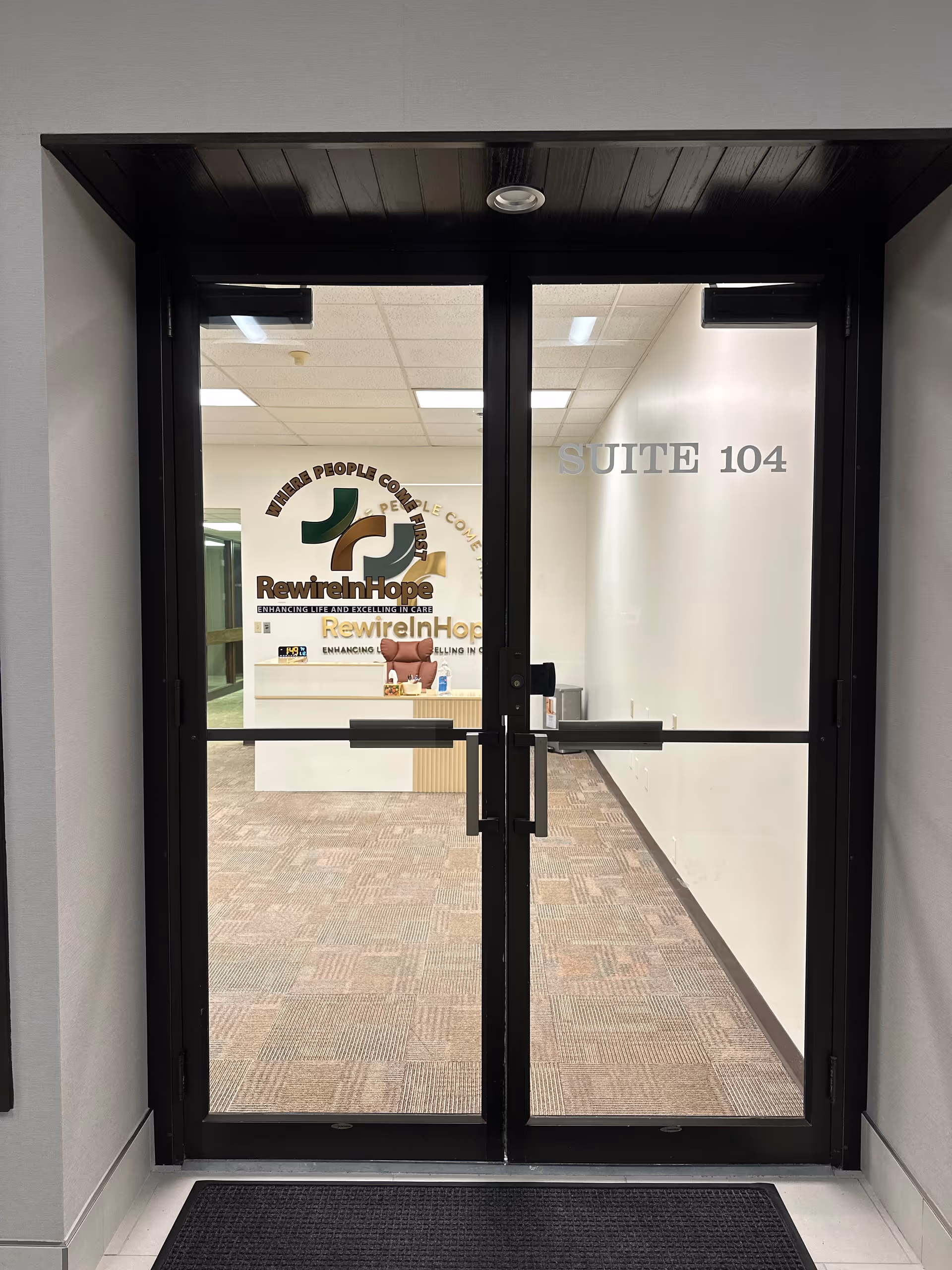Double glass doors open into a reception area featuring the RewireInHope logo and Suite 104.