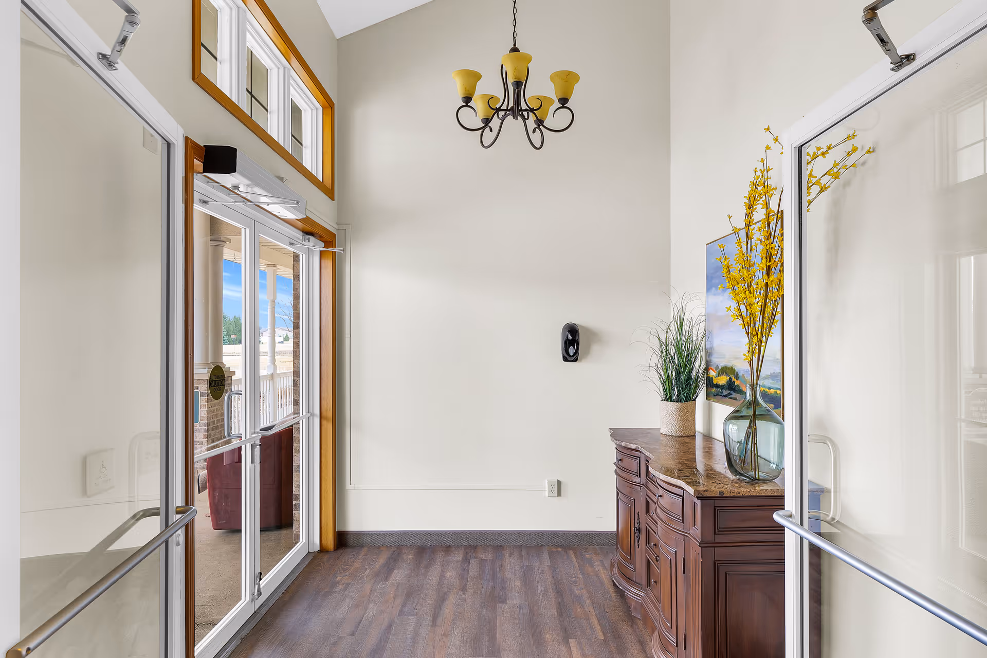 Bright entry hallway with glass doors, a console table, and decorative vase and chandelier.