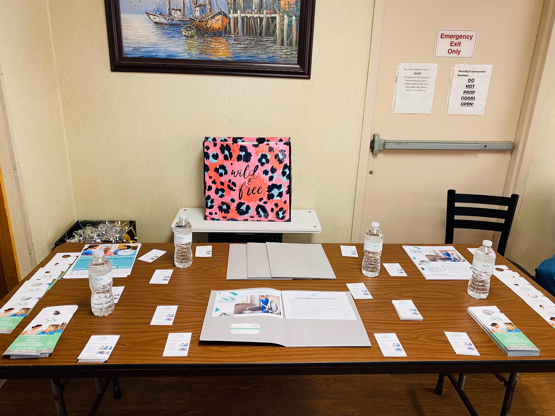 A long table in a room with brochures, water bottles, and a pink tote bag.