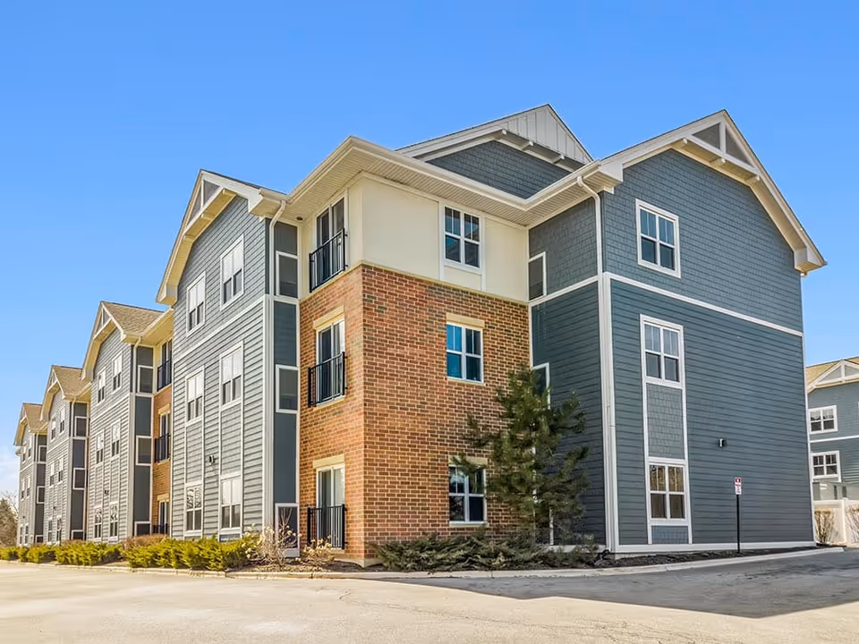 Exterior view of a multi-story residential building with blue siding and brick accents under a clear blue sky.