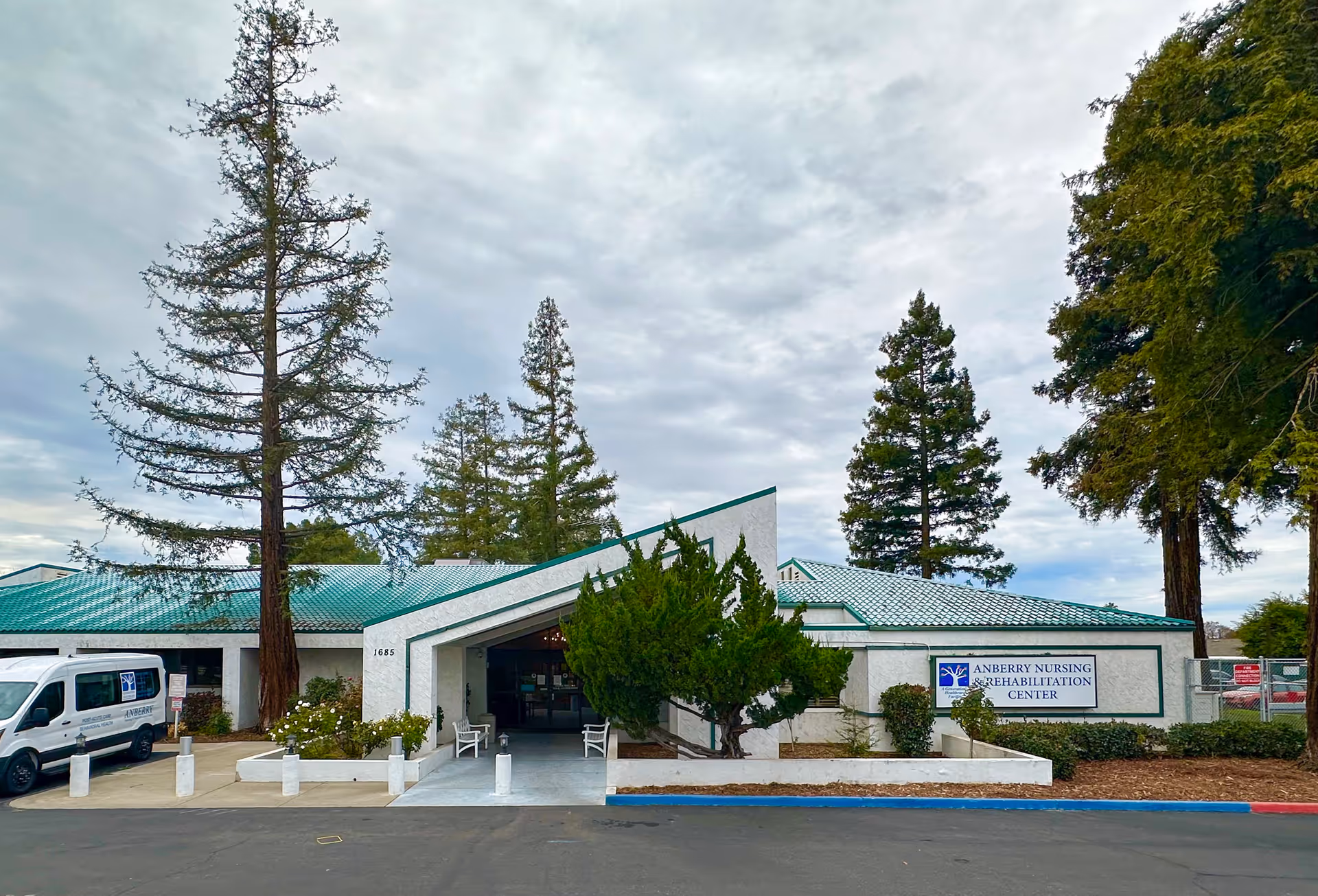 Front view of Anberry Nursing and Rehabilitation Center with entrance, sign, and tall trees.