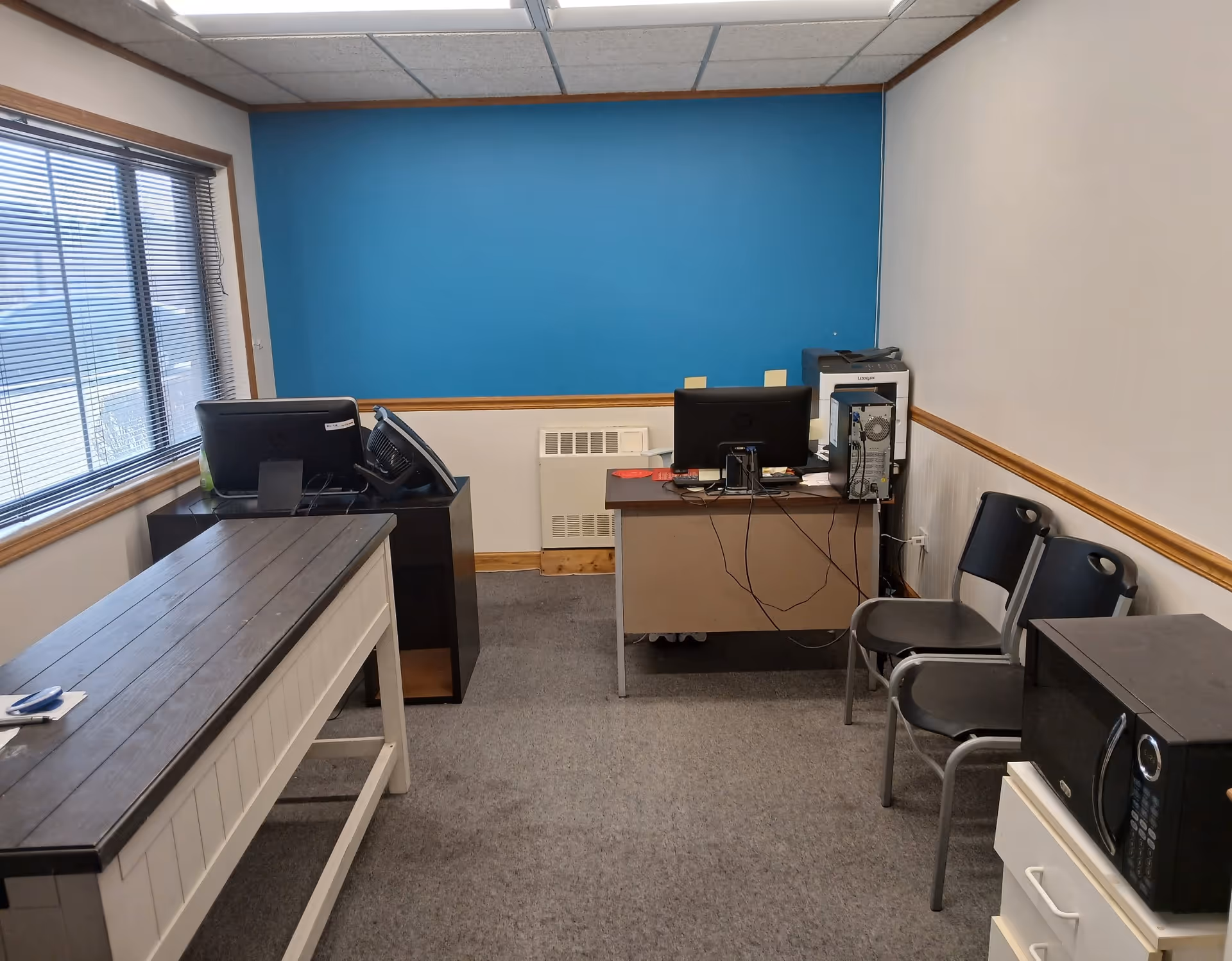 Office workspace in a senior care facility with blue accent wall, desks, computers, printer, and chairs.