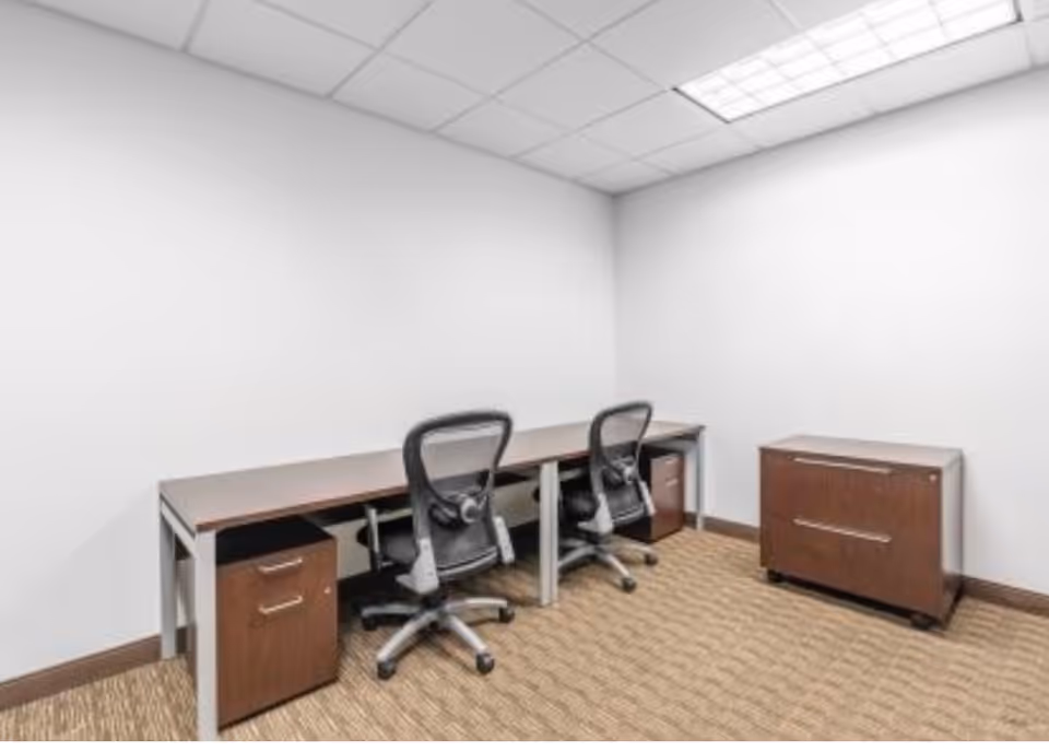 Small office area with two desks, chairs, and filing cabinets in a bare room.