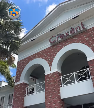 Brick building with white arches and balconies, palm tree nearby, Silver Caregivers logo visible.