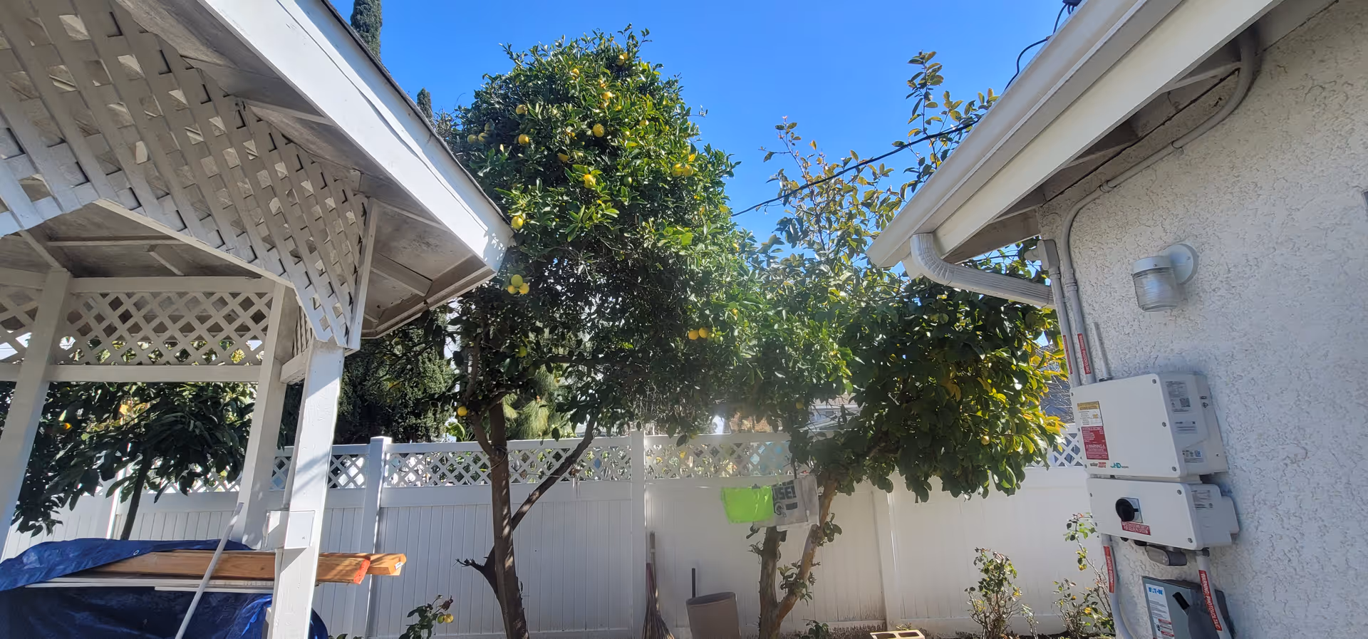 Exterior outdoor area with a white fence, trees, and utility meters beside the building.