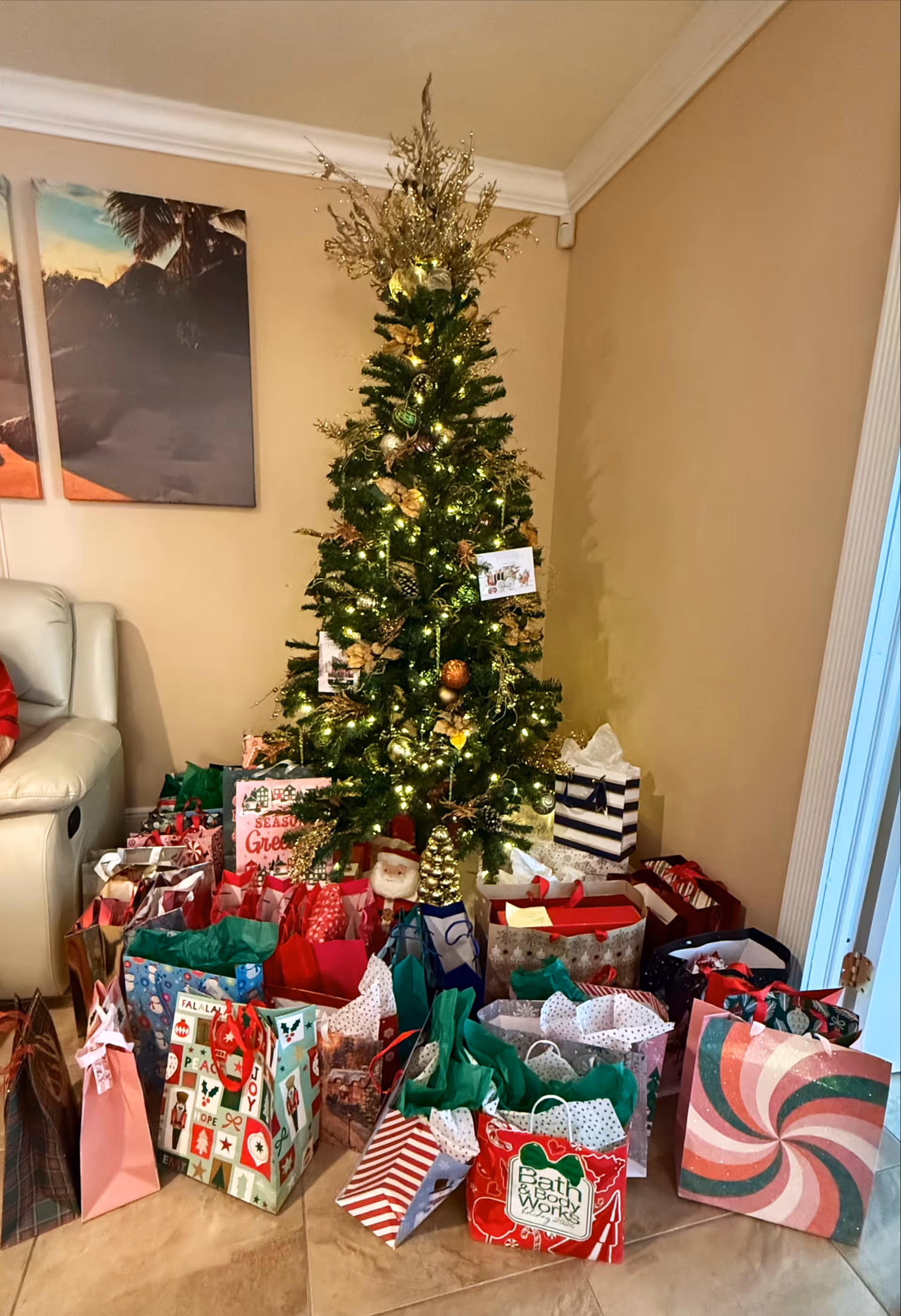 A decorated Christmas tree with numerous gift bags sits in a living room.