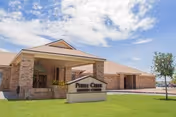 Brick nursing center exterior with covered entrance and Pebble Creek Nursing Center sign under blue sky.