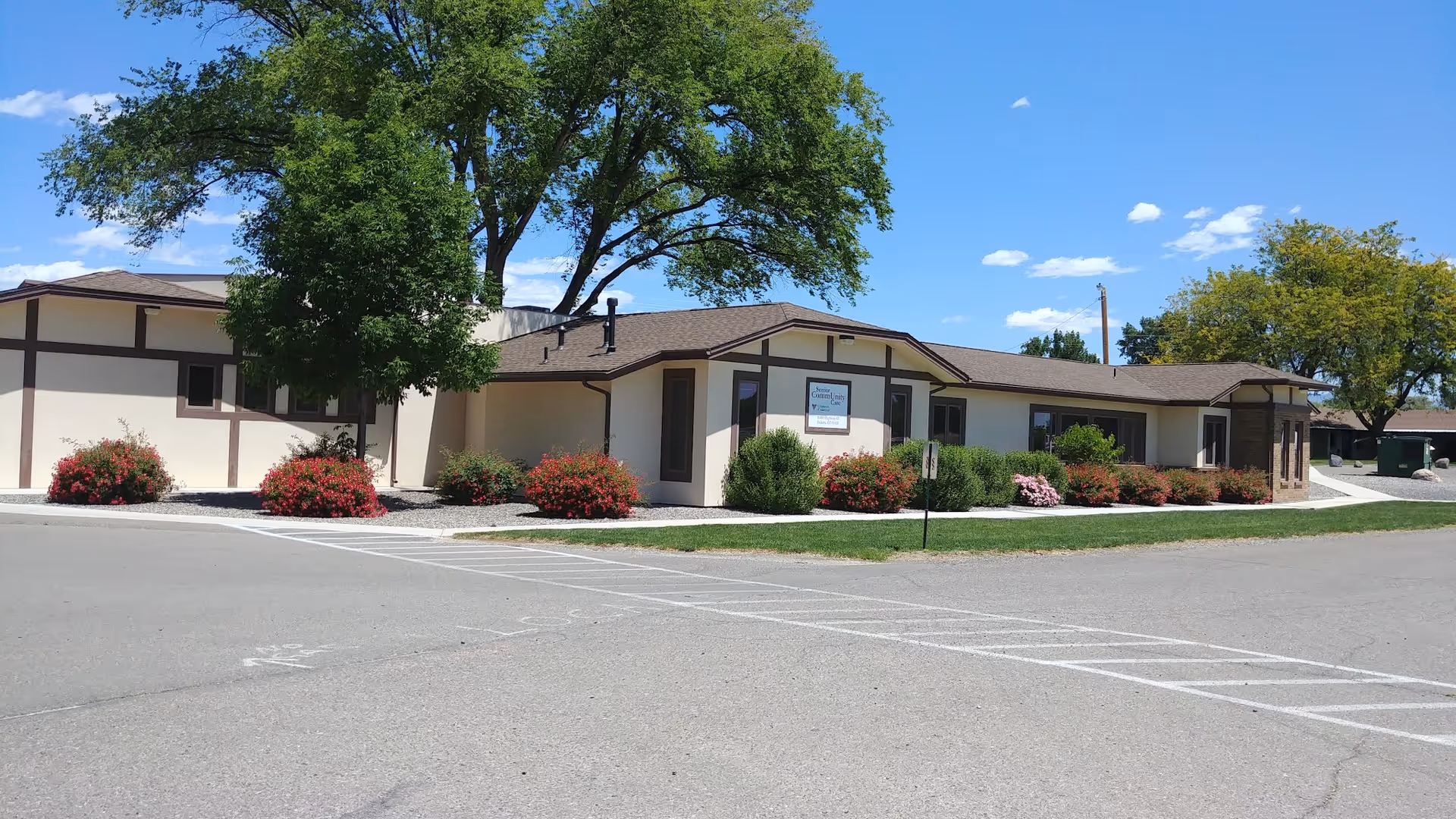 One-story beige building with brown trim, landscaped shrubs, and a large tree near the entrance.
