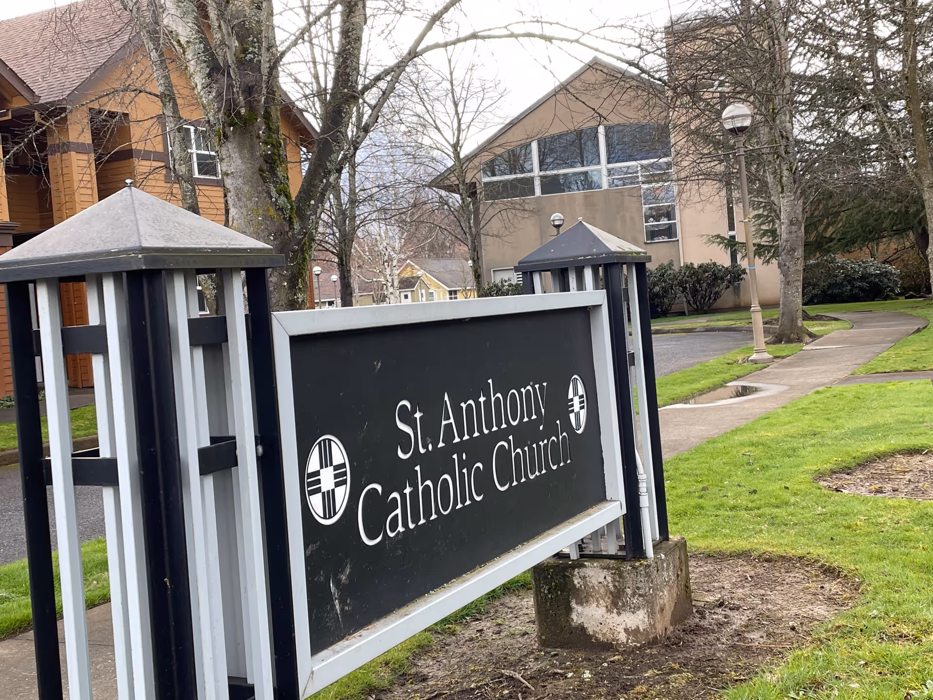 Outdoor sign reading St. Anthony Catholic Church with adjacent buildings and greenery.