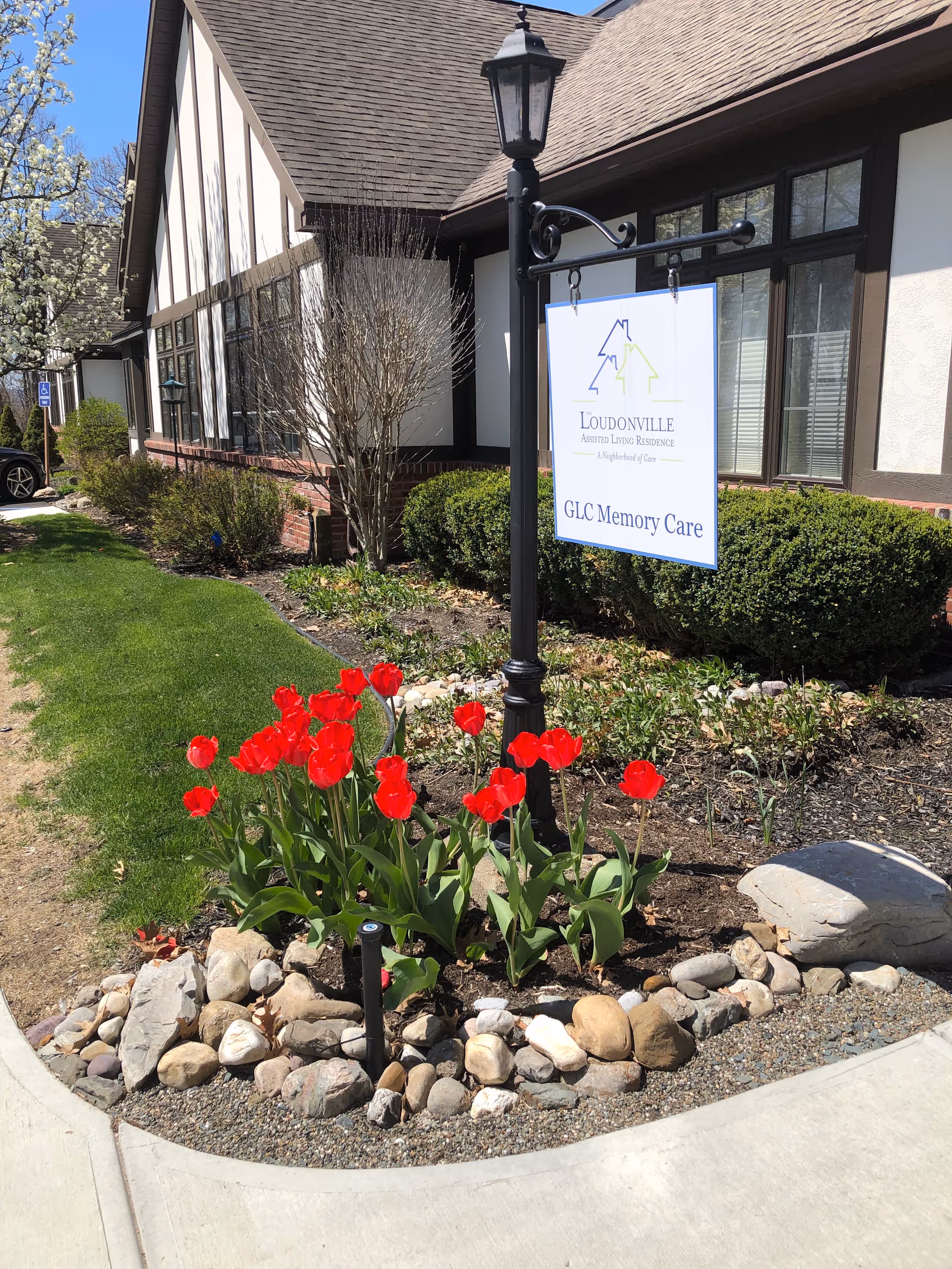 Front exterior of Loudonville Assisted Living Residence with sign, landscaping and red tulips.