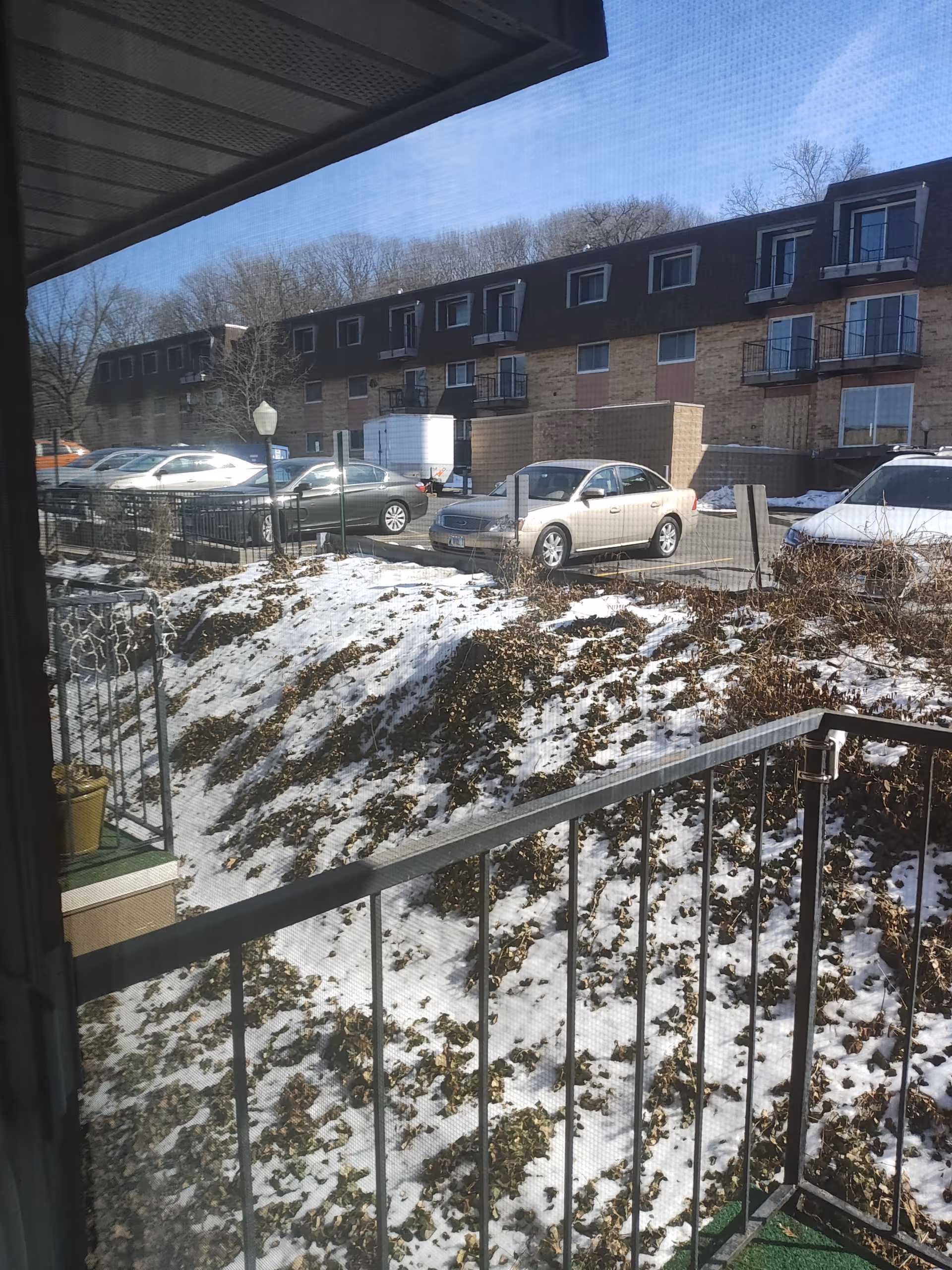 Outdoor view from a Friendship Manor balcony: snow-covered slope, cars in parking lot, building with balconies.