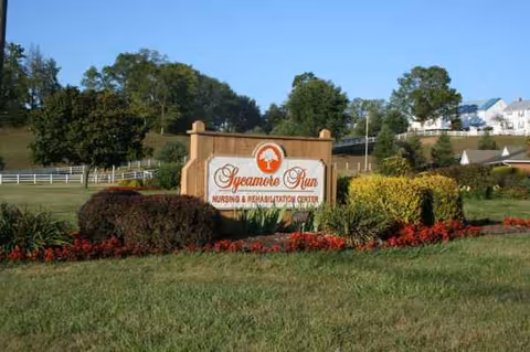 Front stone sign reading Sycamore Run Nursing and Rehabilitation Center on a landscaped lawn.
