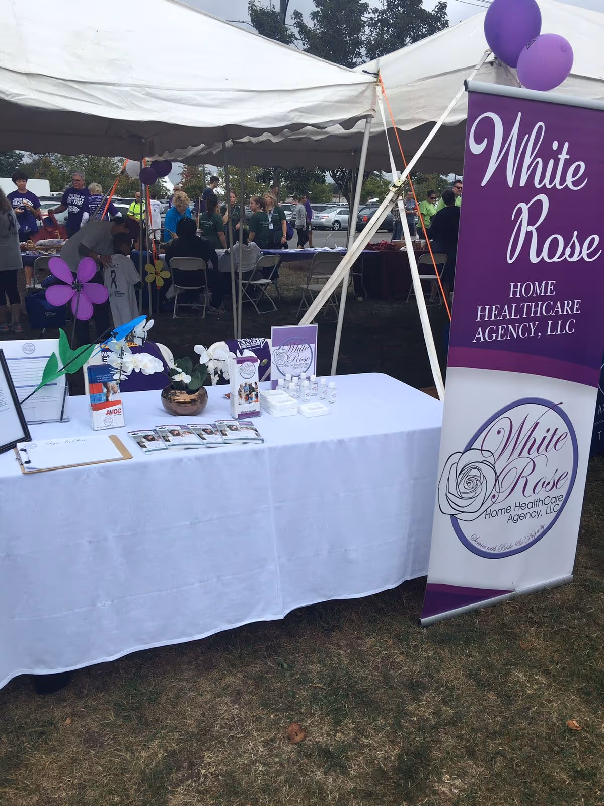Outdoor event booth for White Rose Home Healthcare Agency with tables and attendees.