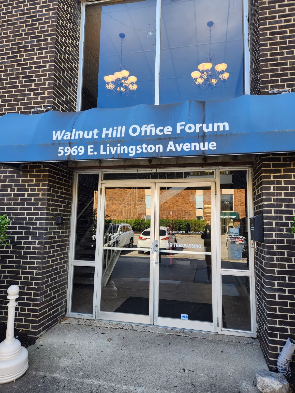 Brick building entrance with glass doors and a blue canopy reading Walnut Hill Office Forum.