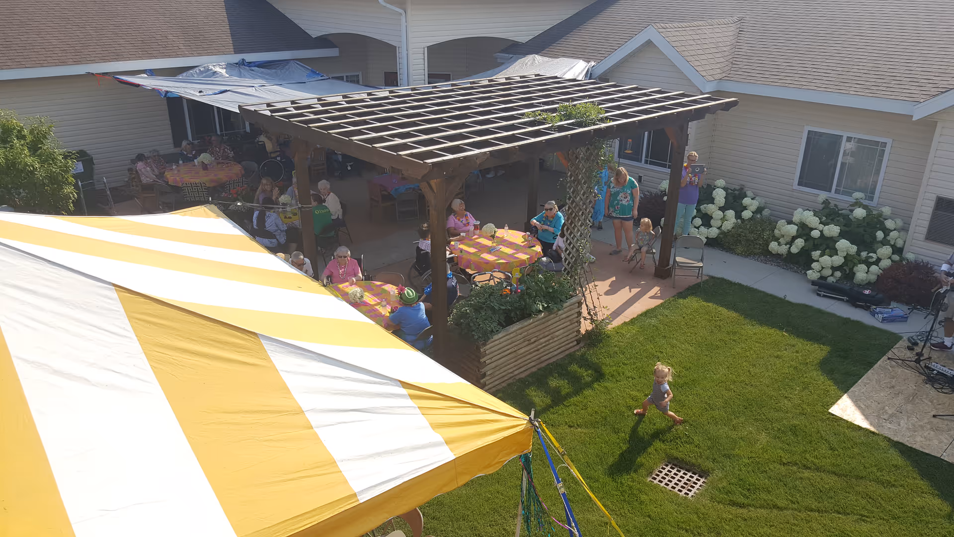 Outdoor courtyard at Serenity Living Center with tents, tables, residents seated, child running.