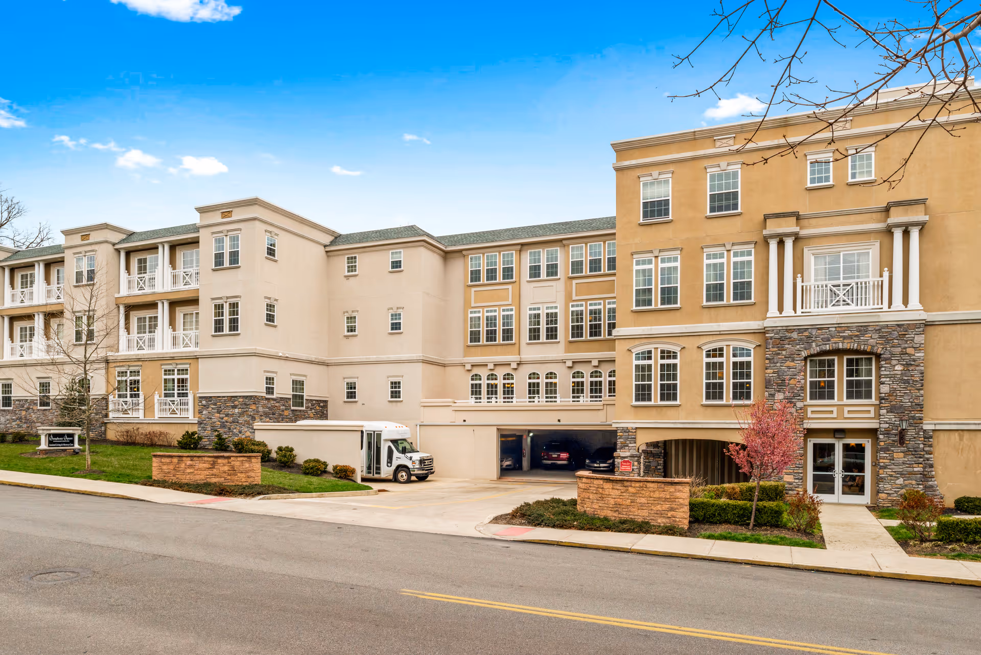 Exterior view of Symphony Square senior living facility with beige stucco, stone accents, and driveway.