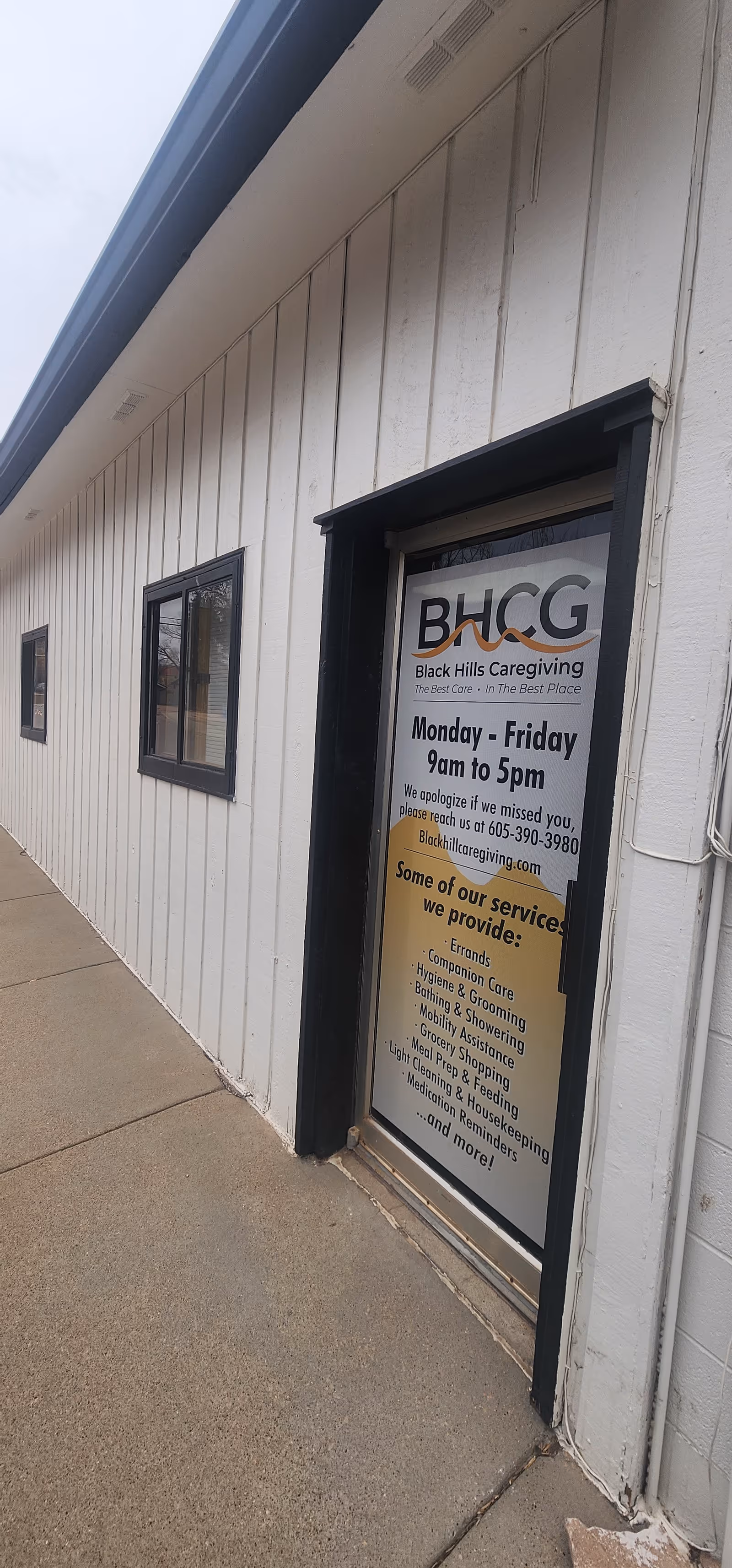 Exterior of a white facility wall with BHCG entrance door and posted hours.