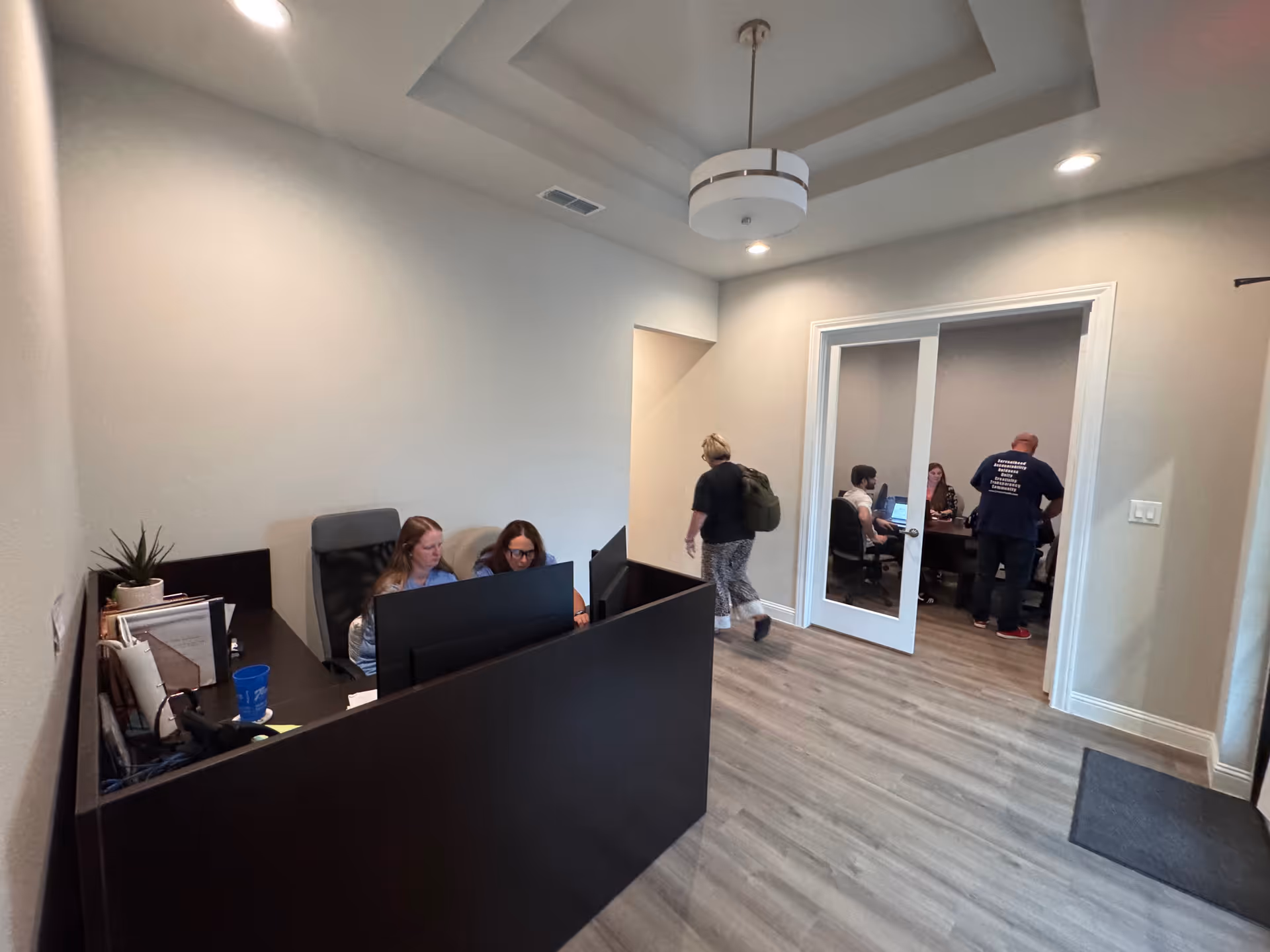 Interior reception area with staff at a dark desk and people in a conference room.