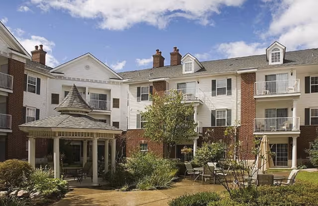 Three-story brick-and-white siding senior living building with balconies surrounding a landscaped courtyard and a gazebo.