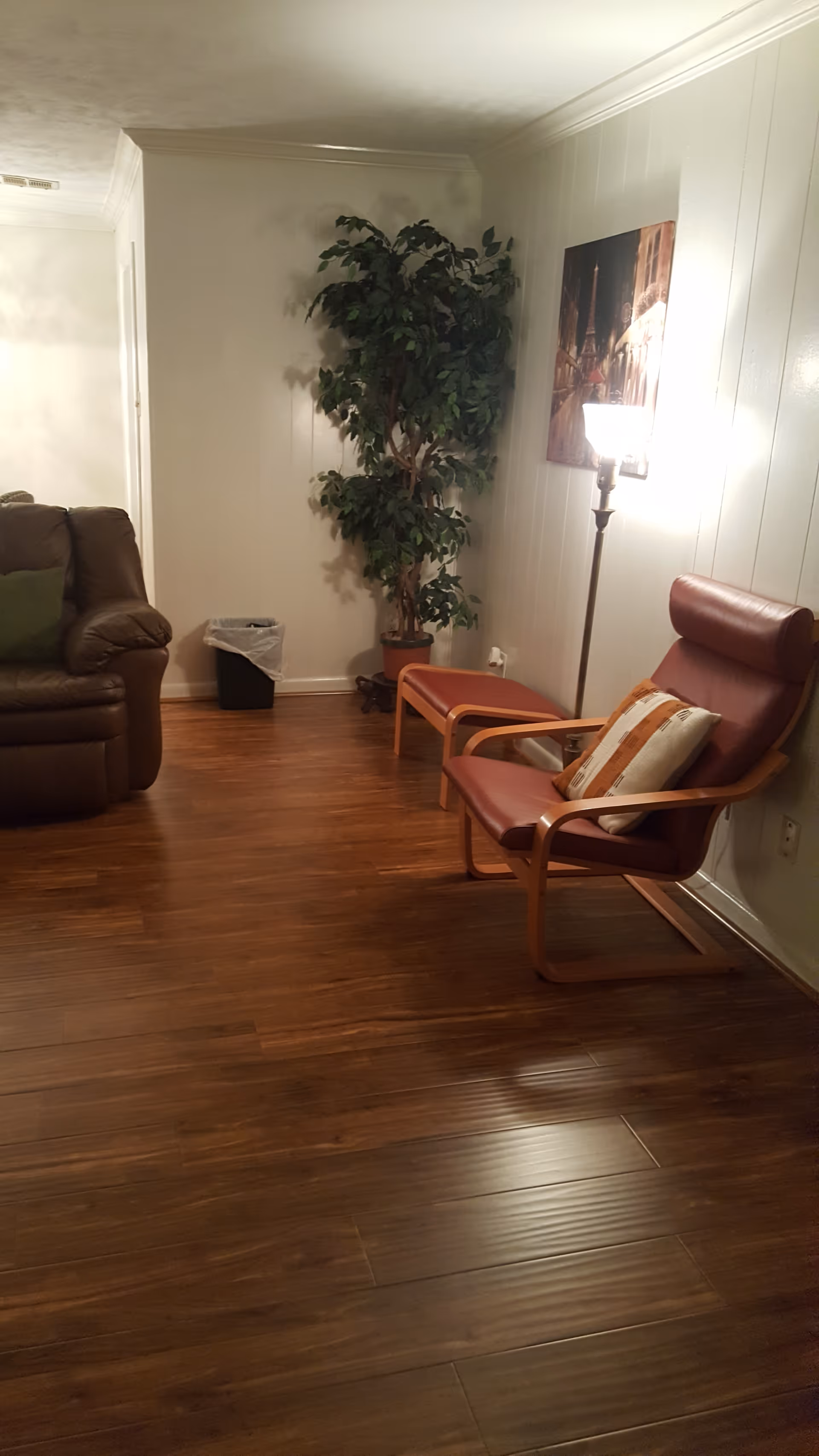 Cozy living room with brown leather chair, plant, lamp, and wall art.
