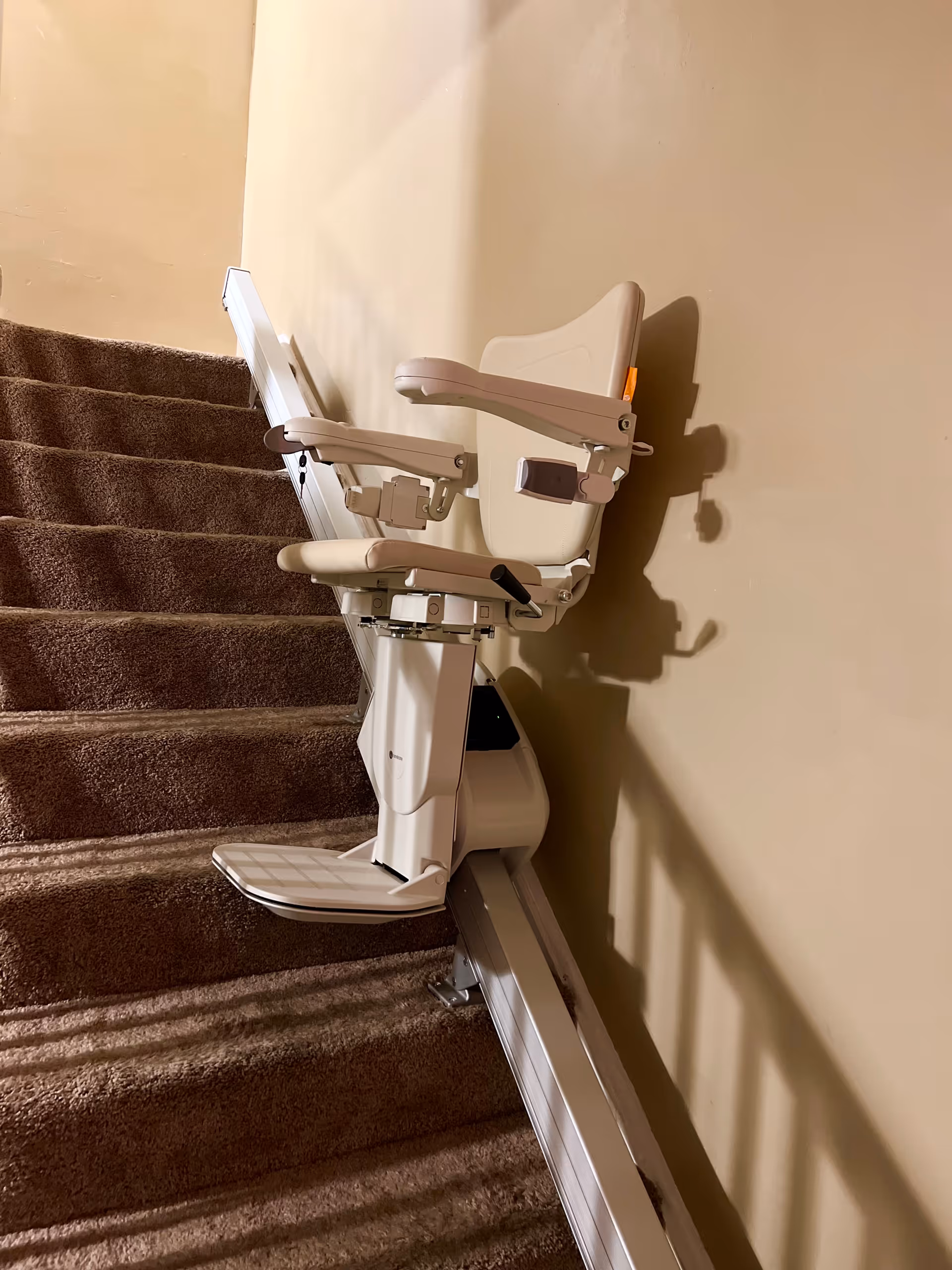 A white stair lift installed along carpeted stairs in an interior hallway.