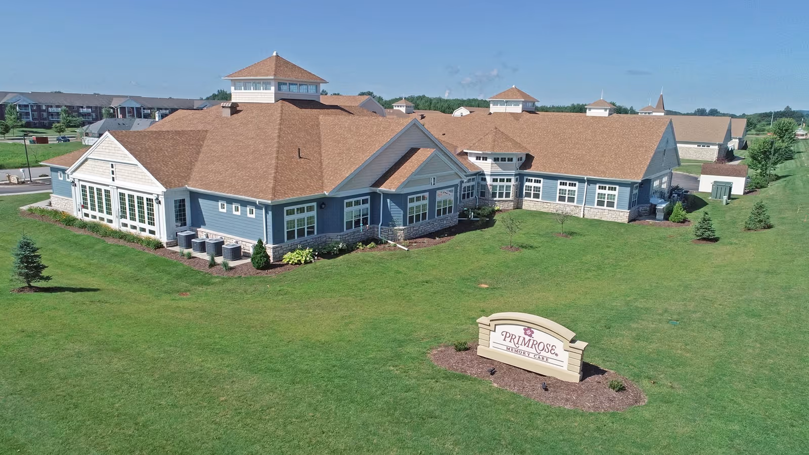 A sprawling retirement campus with blue buildings, manicured lawn, and a front sign.