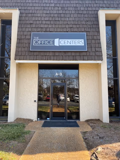 Front entrance of a beige building with a sign reading The Office Centers above doors.