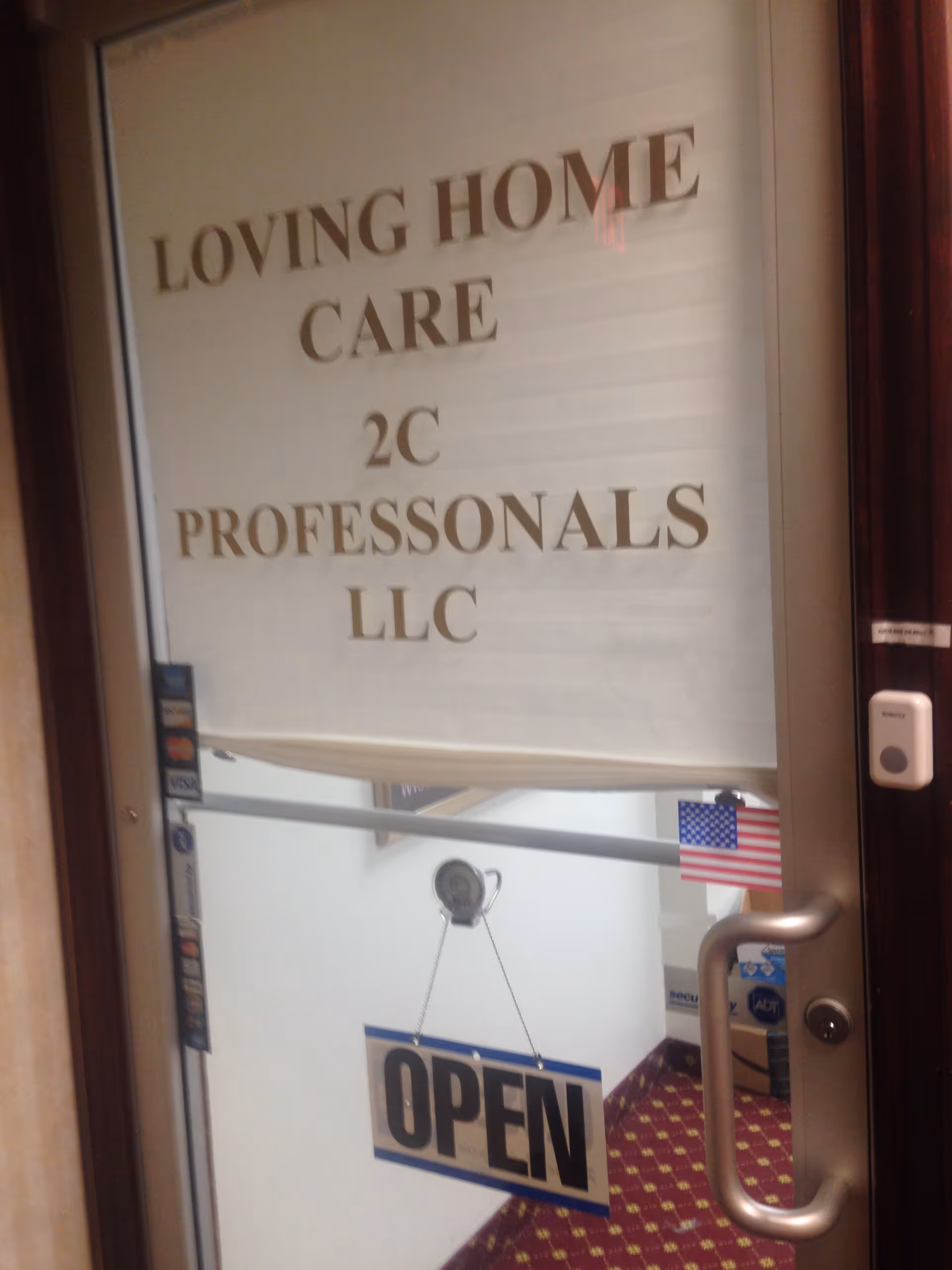 Glass door with 'Loving Home Care Professionals LLC' sign and OPEN sign inside a carpeted hallway.