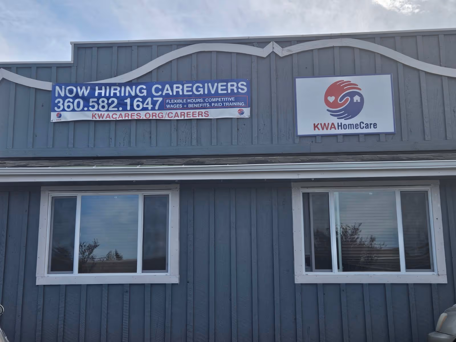 Front of blue building with two windows and Now Hiring Caregivers banners.