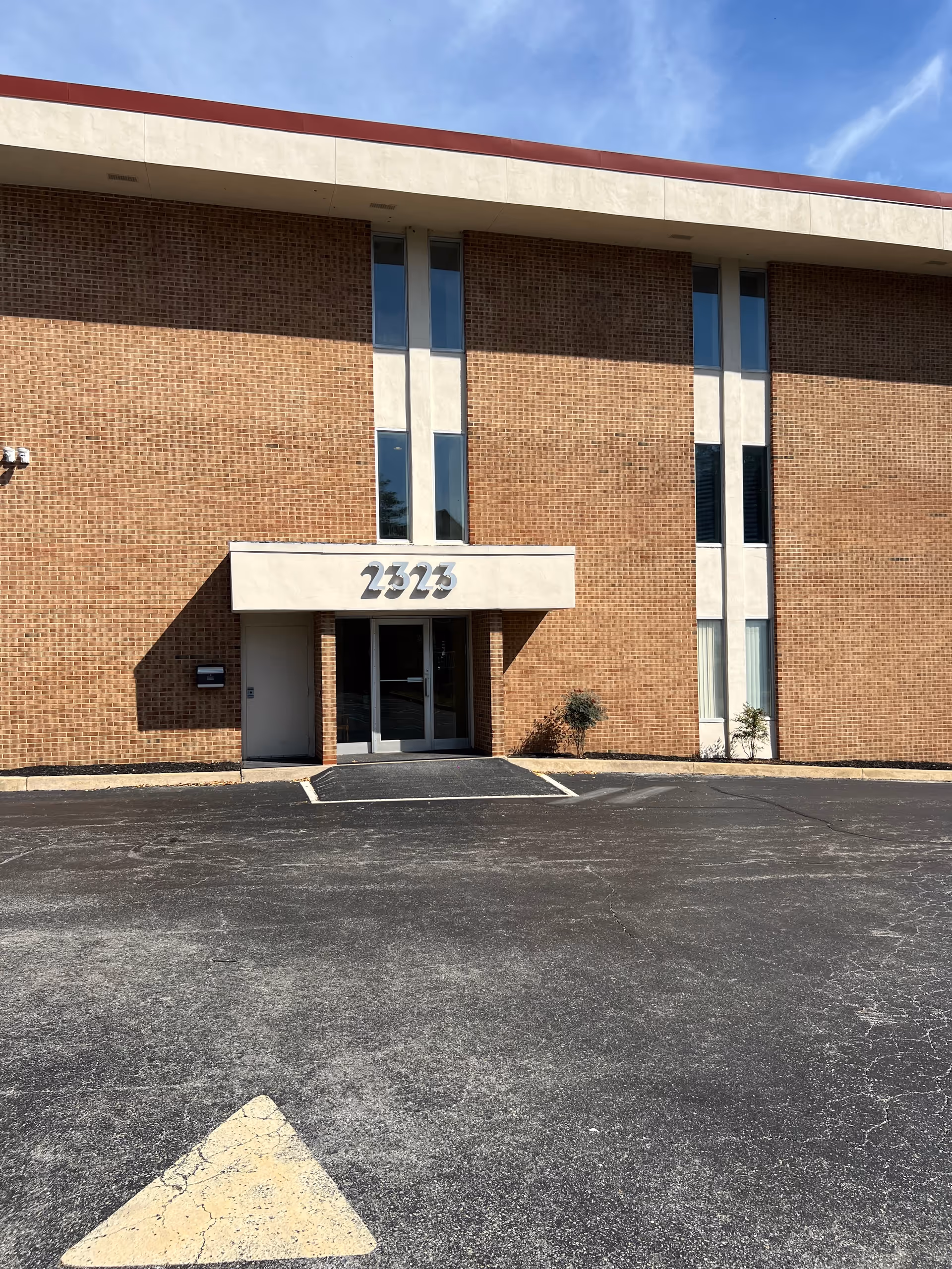 Brick building with glass entrance and marked parking area in the foreground.