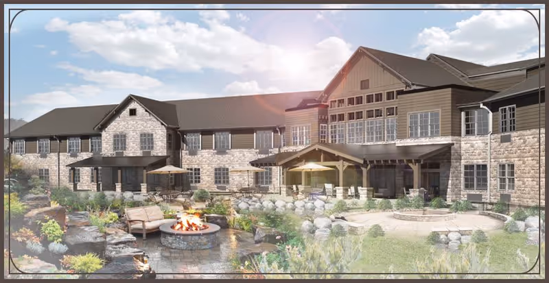 Exterior view of a large senior living facility building with stone and wood siding, multiple windows, and a dark roof. The foreground features a landscaped garden area with a stone fire pit surrounded by outdoor seating, patio umbrellas, and greenery under a partly cloudy sky.