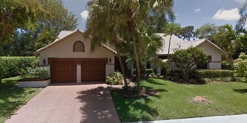 Single-story beige facility with two wooden garage doors, palm trees, and a manicured front yard.