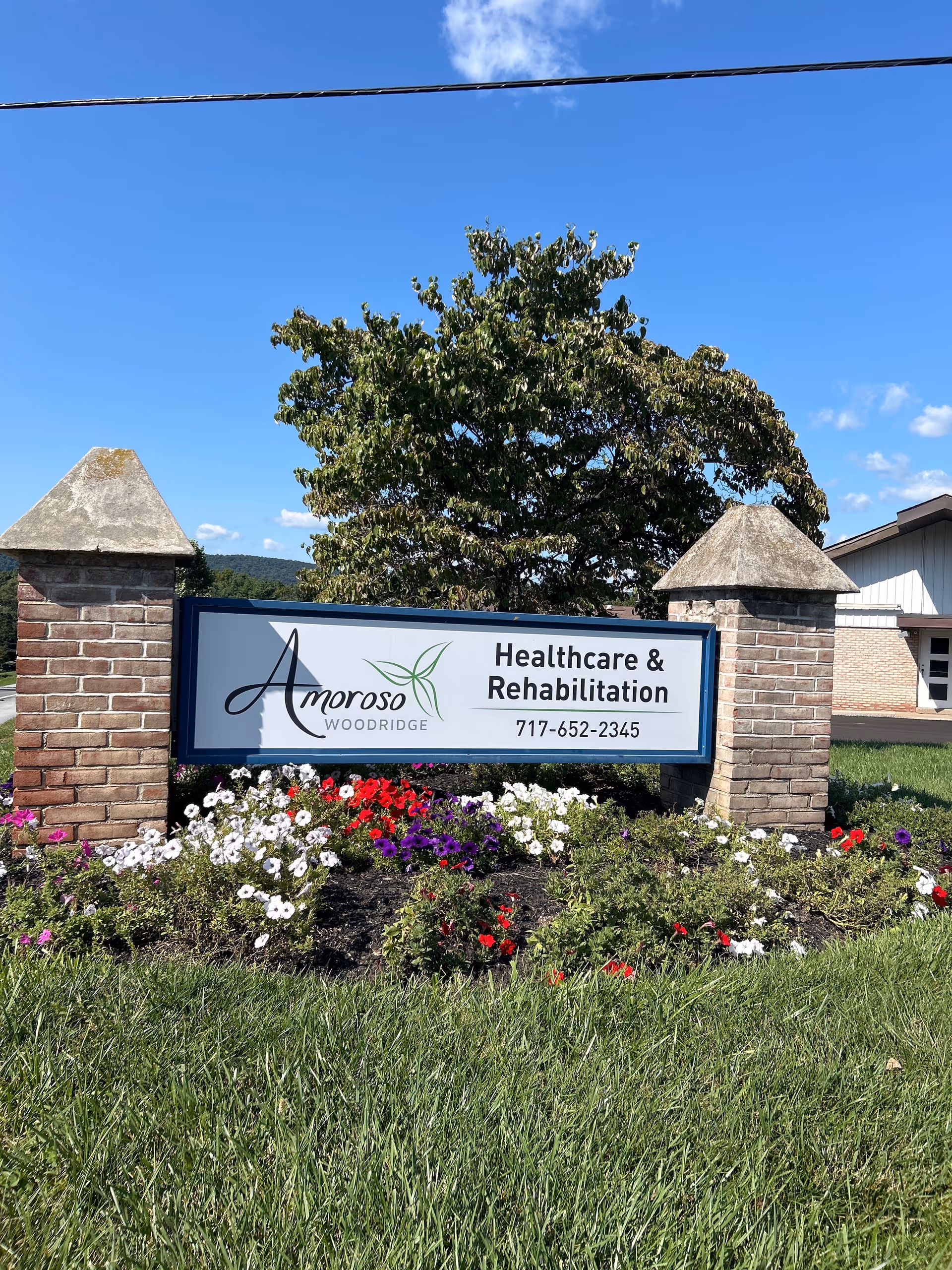 Exterior sign for Amoroso Woodridge Healthcare & Rehabilitation with colorful flower bed