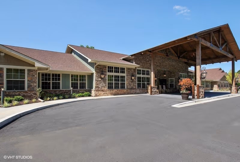 Exterior view of a senior living facility with stone facade and large covered entrance.