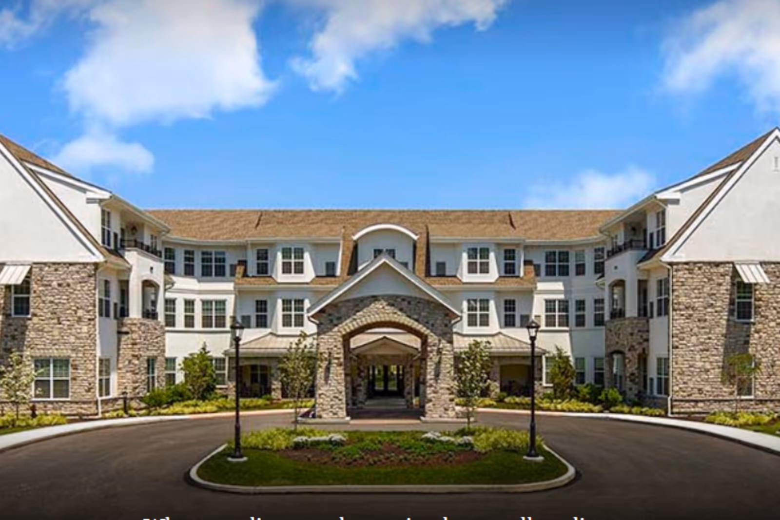 Exterior view of a cream-colored senior living building with stone accents and landscaped entrance.
