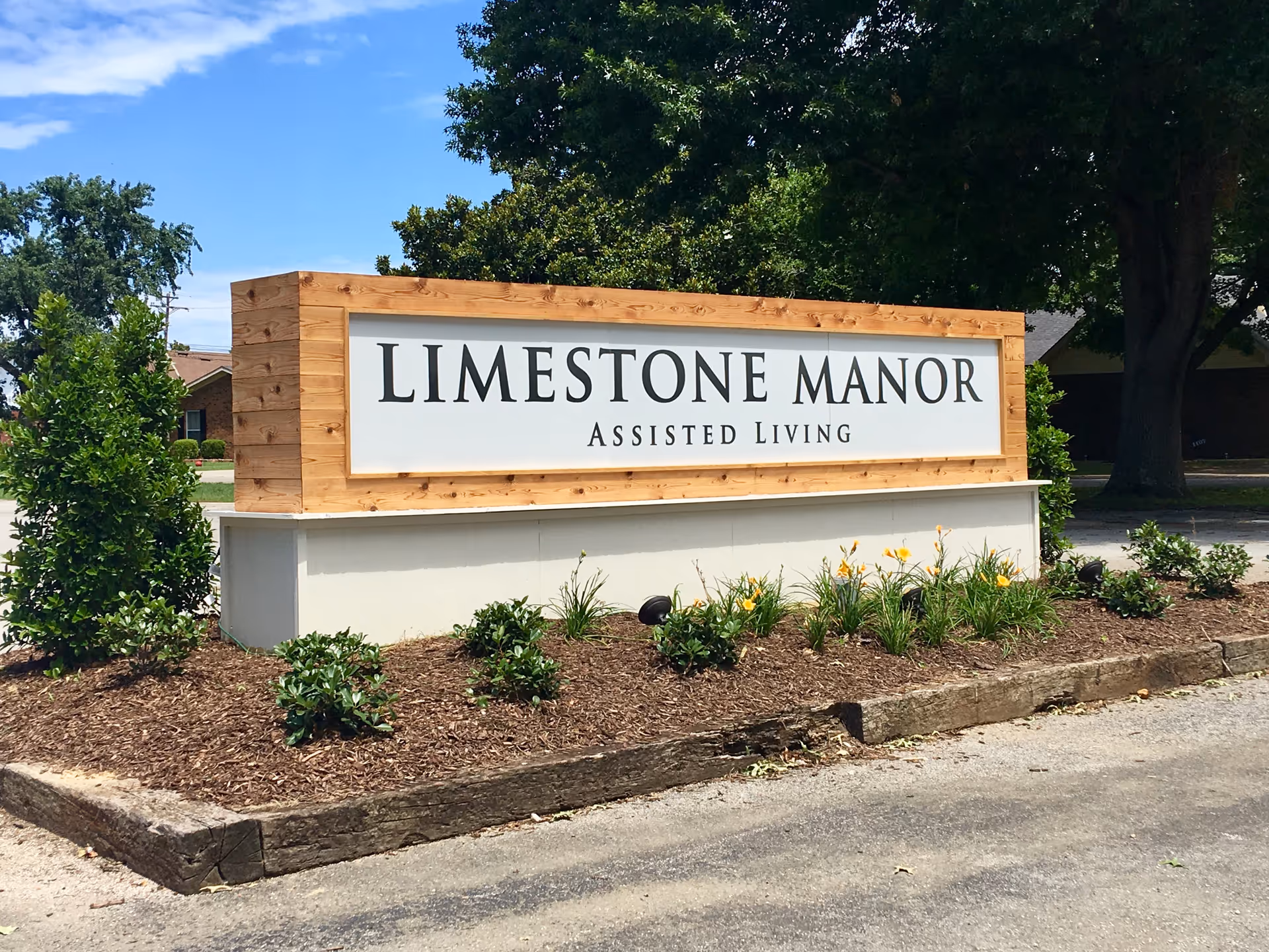 Limestone Manor assisted living sign on a wooden frame with landscaping and trees