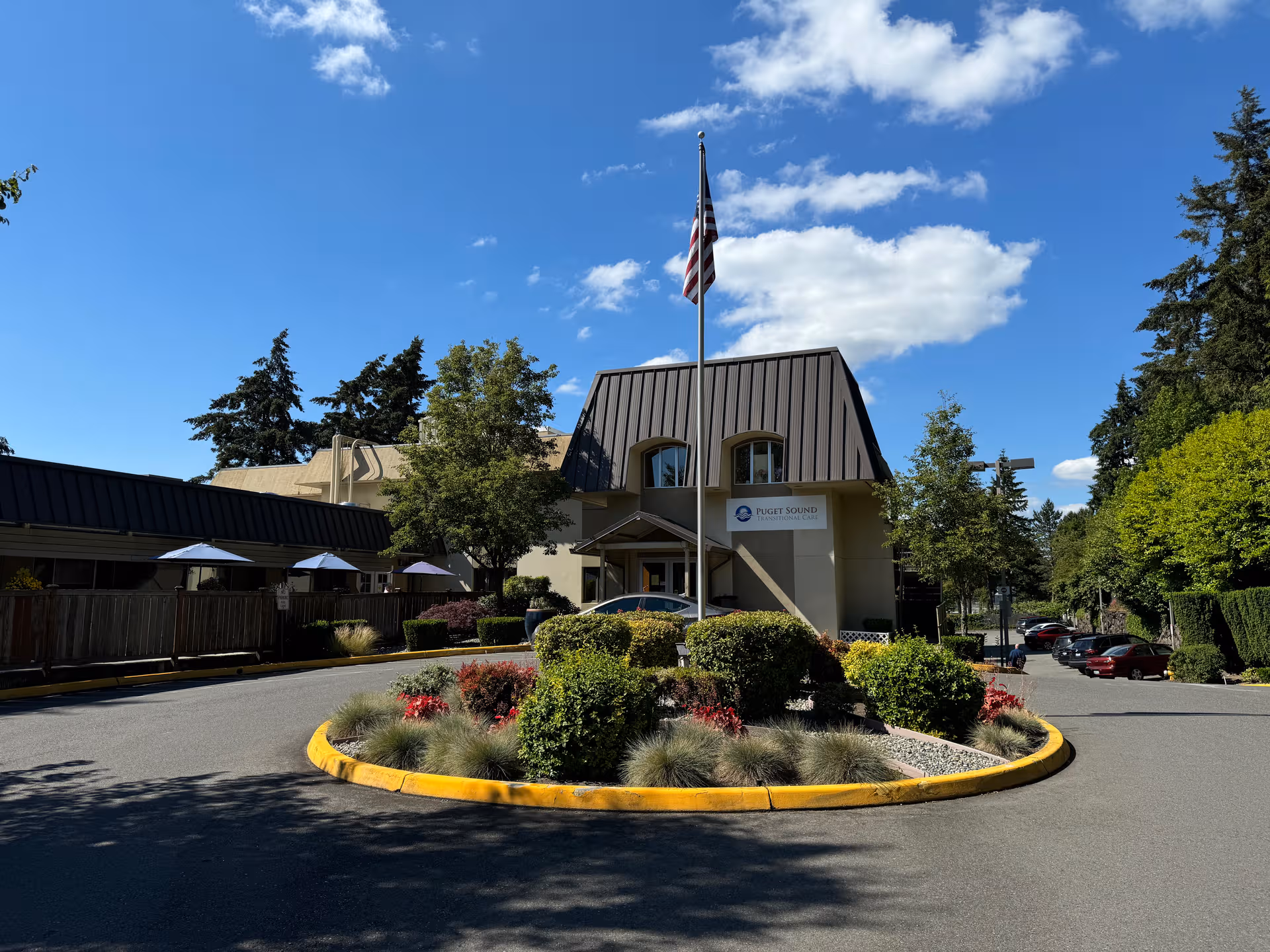 Exterior view of Puget Sound Transitional Care facility with flagpole and landscaped roundabout.