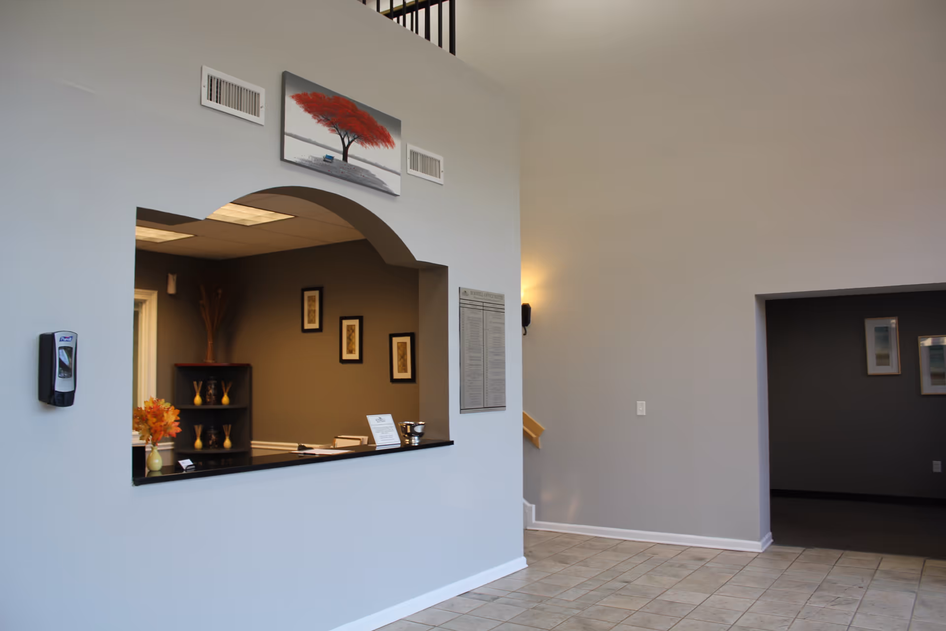 Reception area with a reception window, arch opening, and gray walls in a senior living lobby.